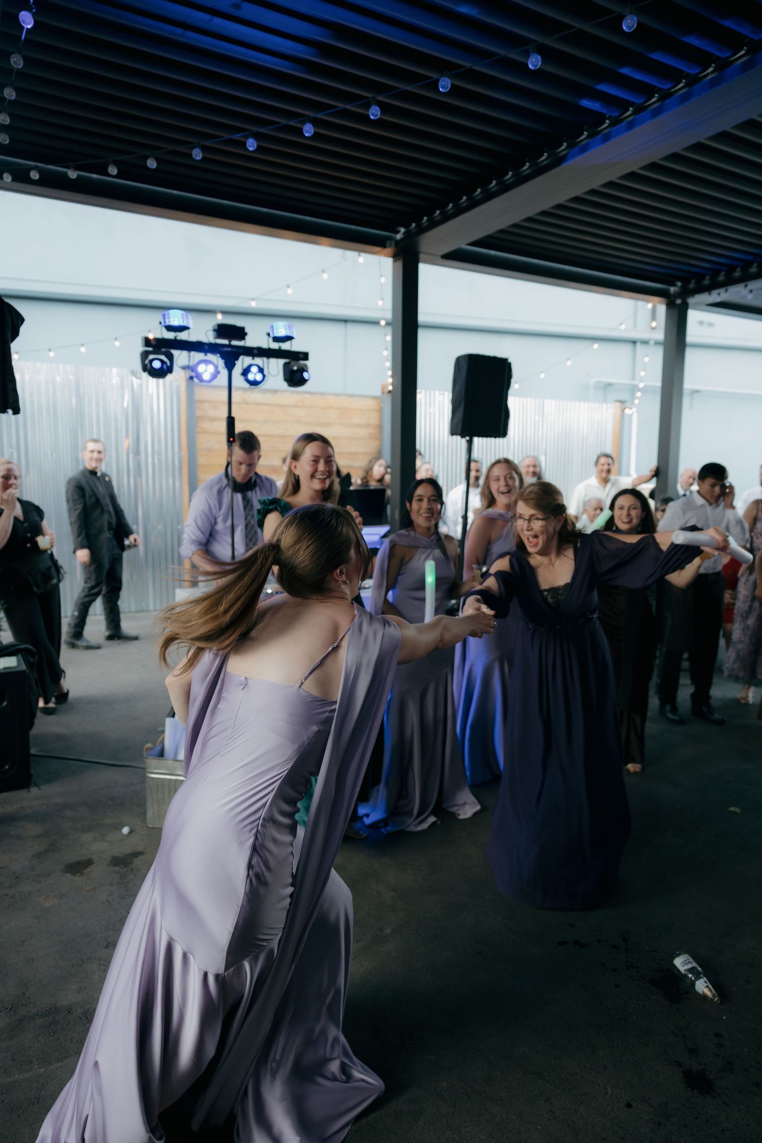Bridesmaid in lavender gown catches bouquet surrounded by excited guests at outdoor wedding reception.