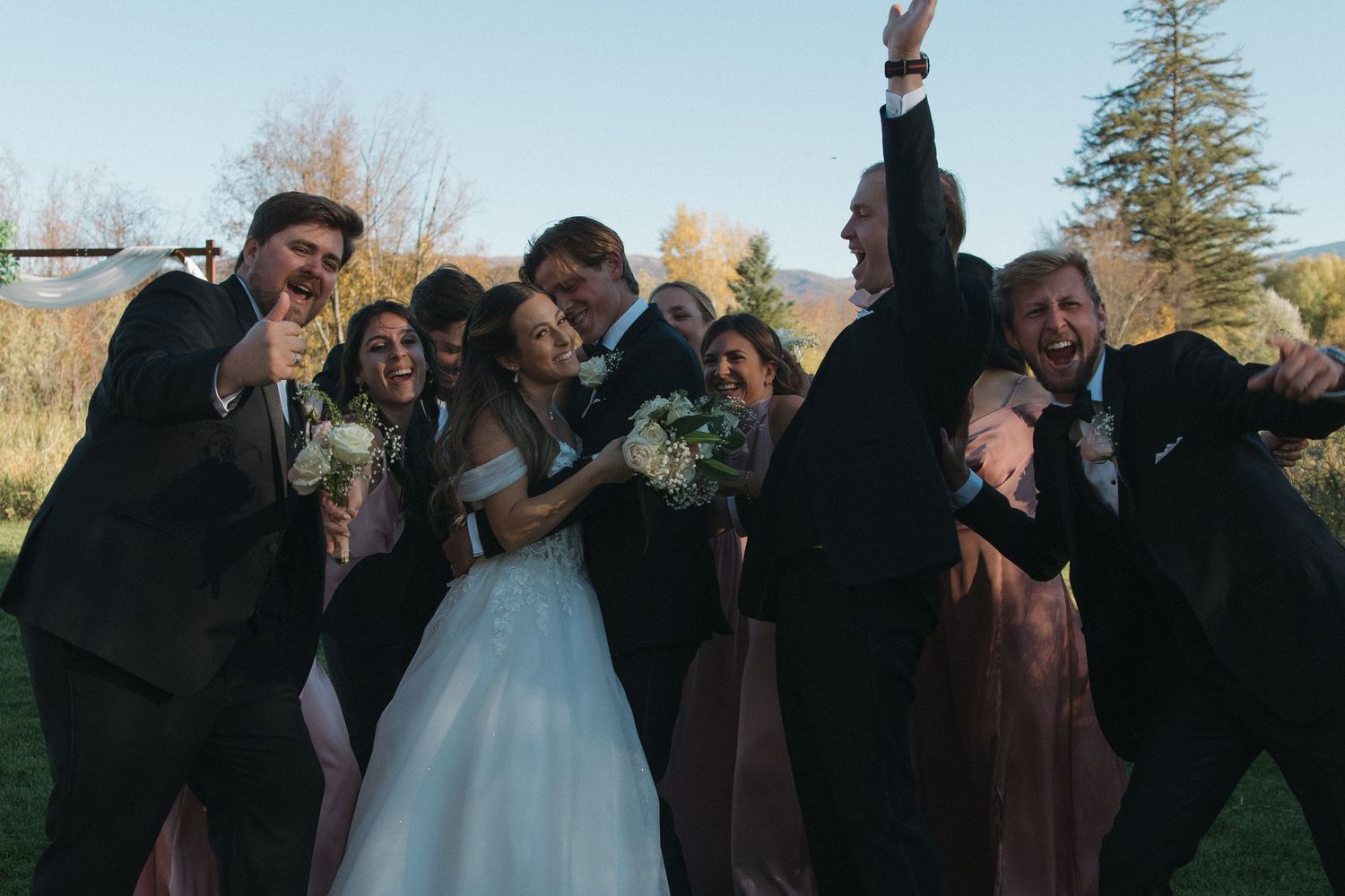 Wedding party poses together for a series of fun and candid group photos outdoors during sunset.