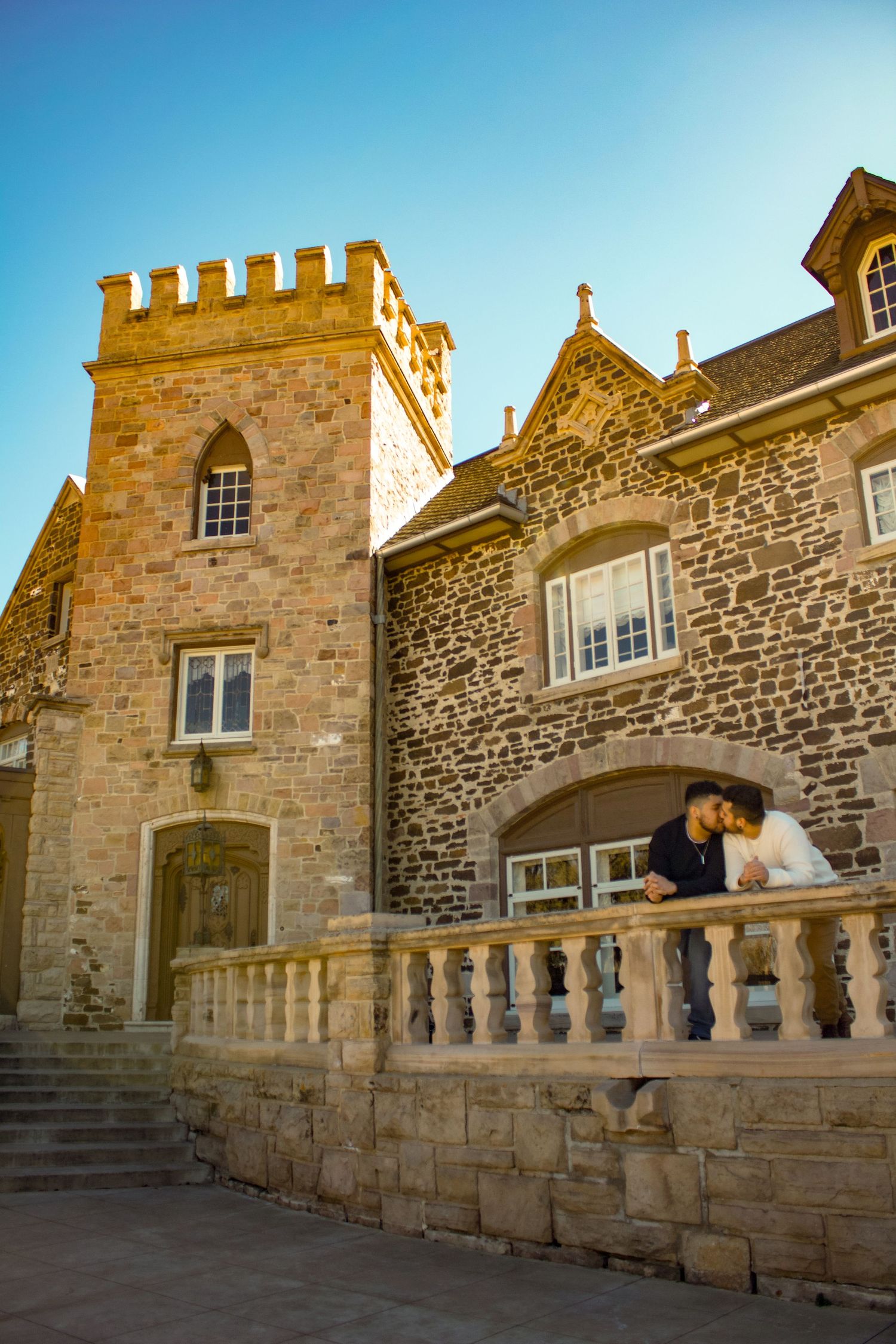 Two people enjoying view from stone balcony of medieval-style architecture.