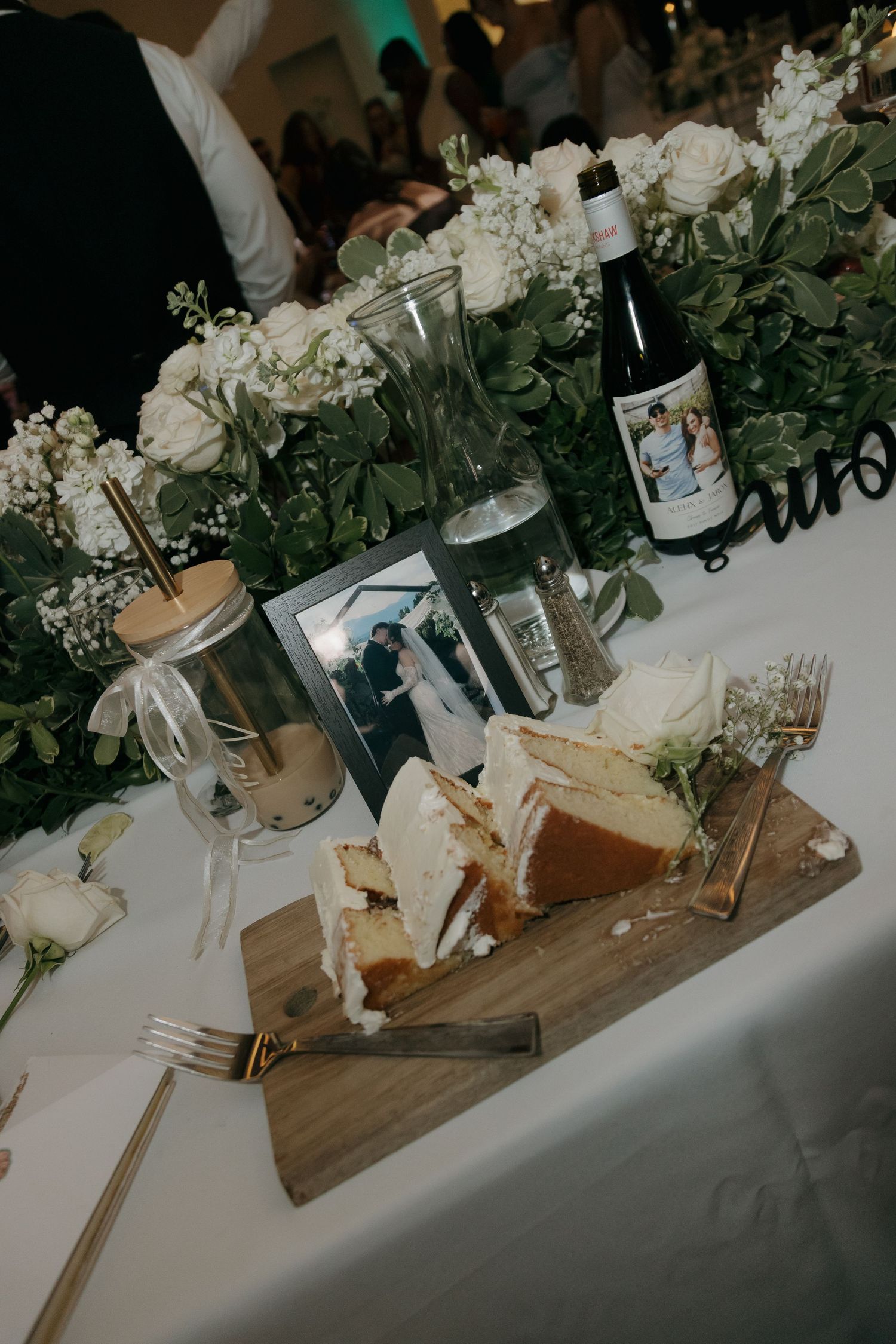 Wedding sweetheart table with white floral centerpiece, cake slices, and couple photo.