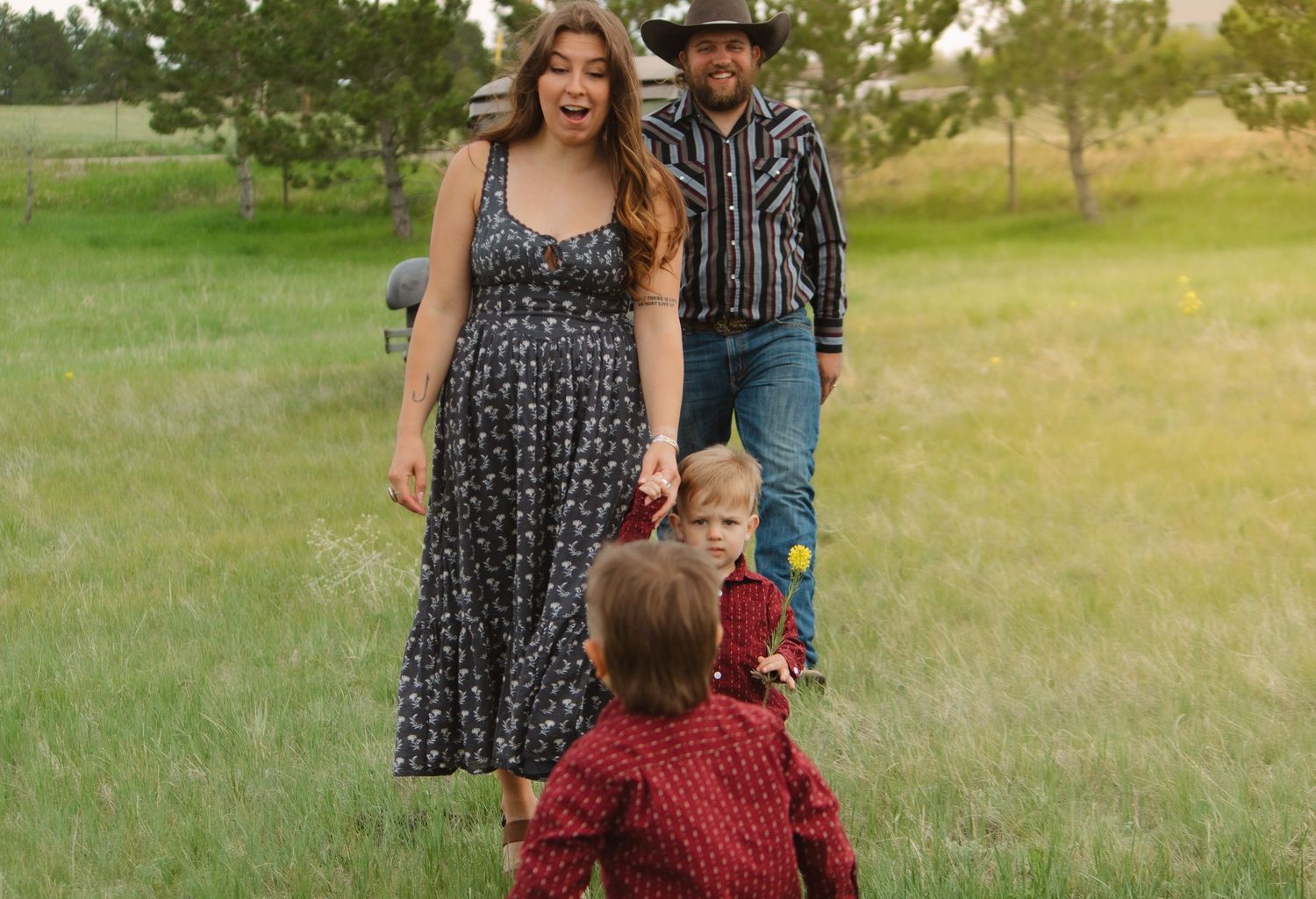 Family wearing coordinating outfits poses together in a grassy field at sunset.
