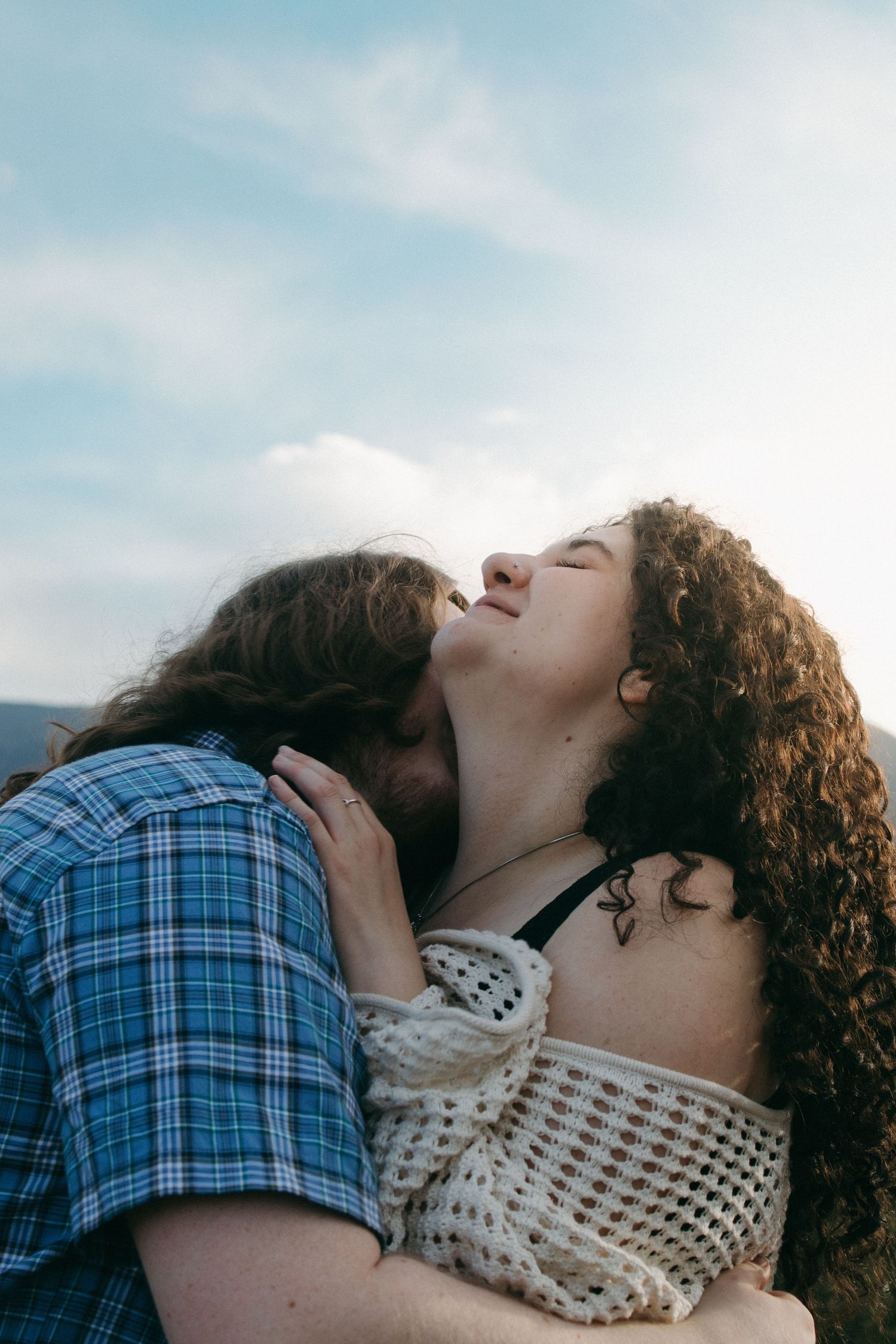 A couple embracing with one wearing plaid and the other in a white crocheted top.