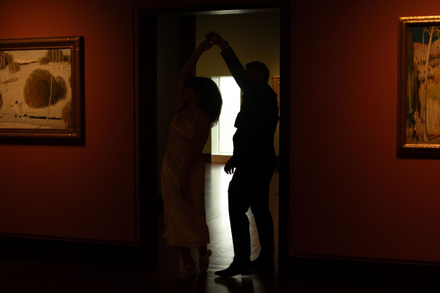 Dark silhouettes against warm gallery lighting create an intimate atmosphere with artwork visible.