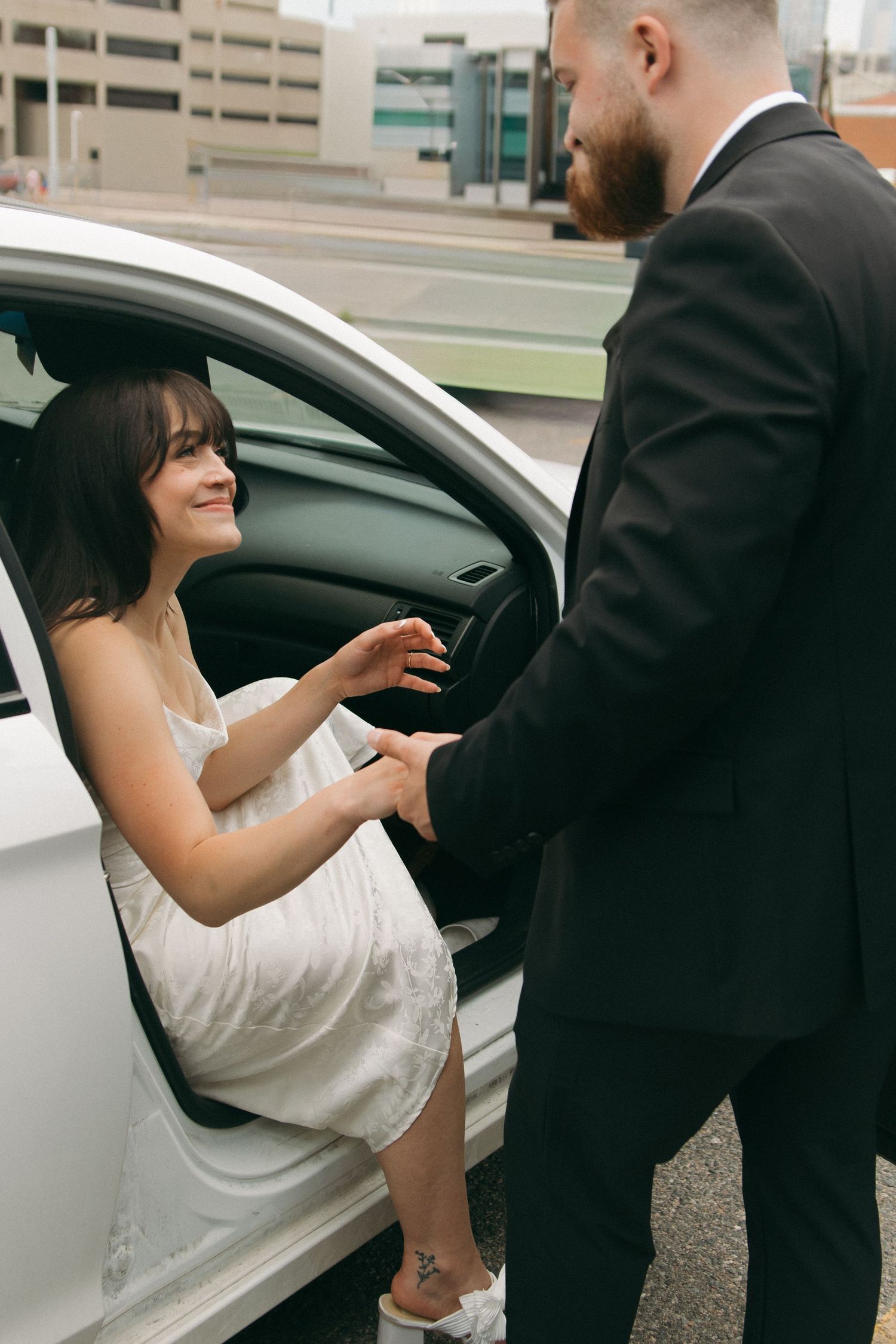 Gentleman helps woman into white car wearing formal attire.