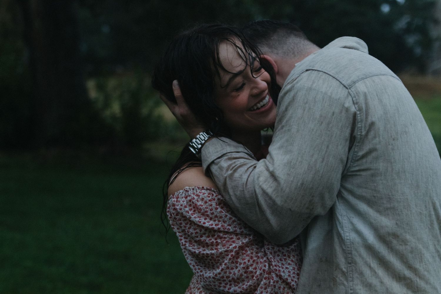A couple shares an intimate embrace while sitting outdoors in casual attire.