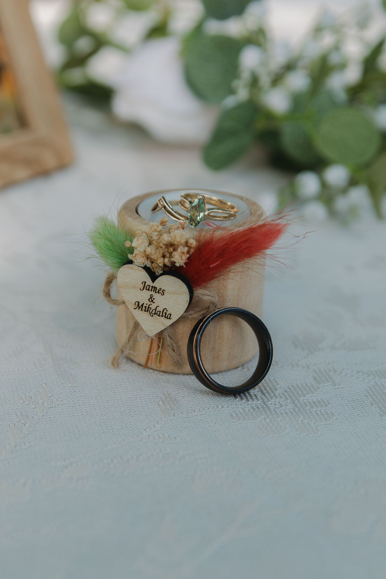 Delicate wedding rings displayed with dried flowers and lace on a light blue textured surface.