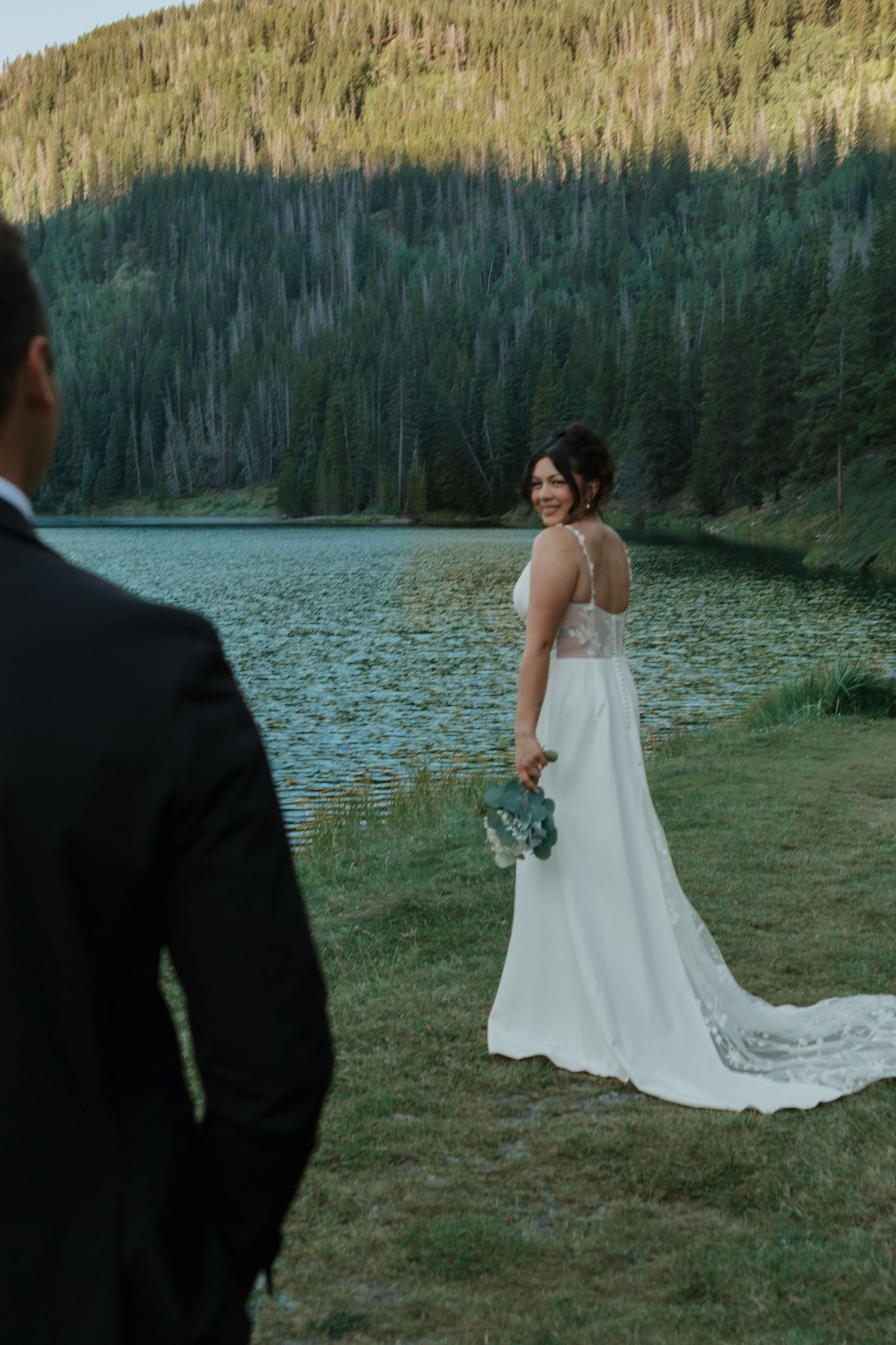 Wedding dress flowing in breeze by scenic mountain lake.