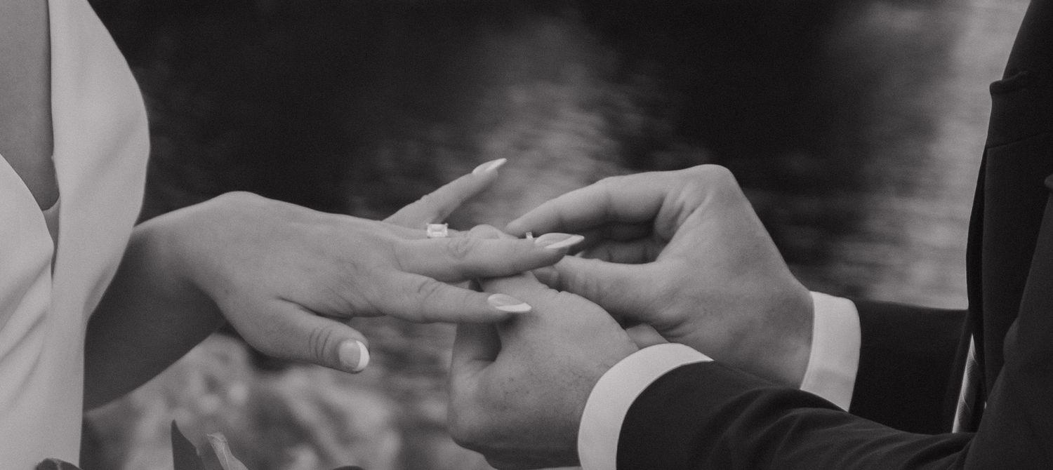 Hands exchange wedding vow books during an intimate ceremony captured in black and white.