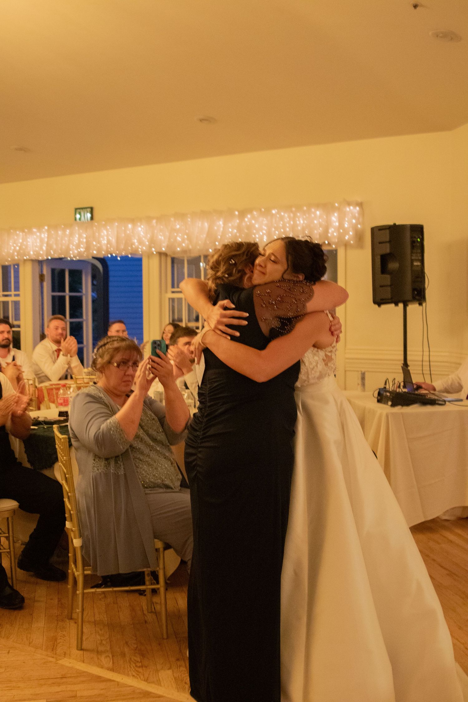 Wedding reception guests dancing and embracing in a warmly lit indoor venue.