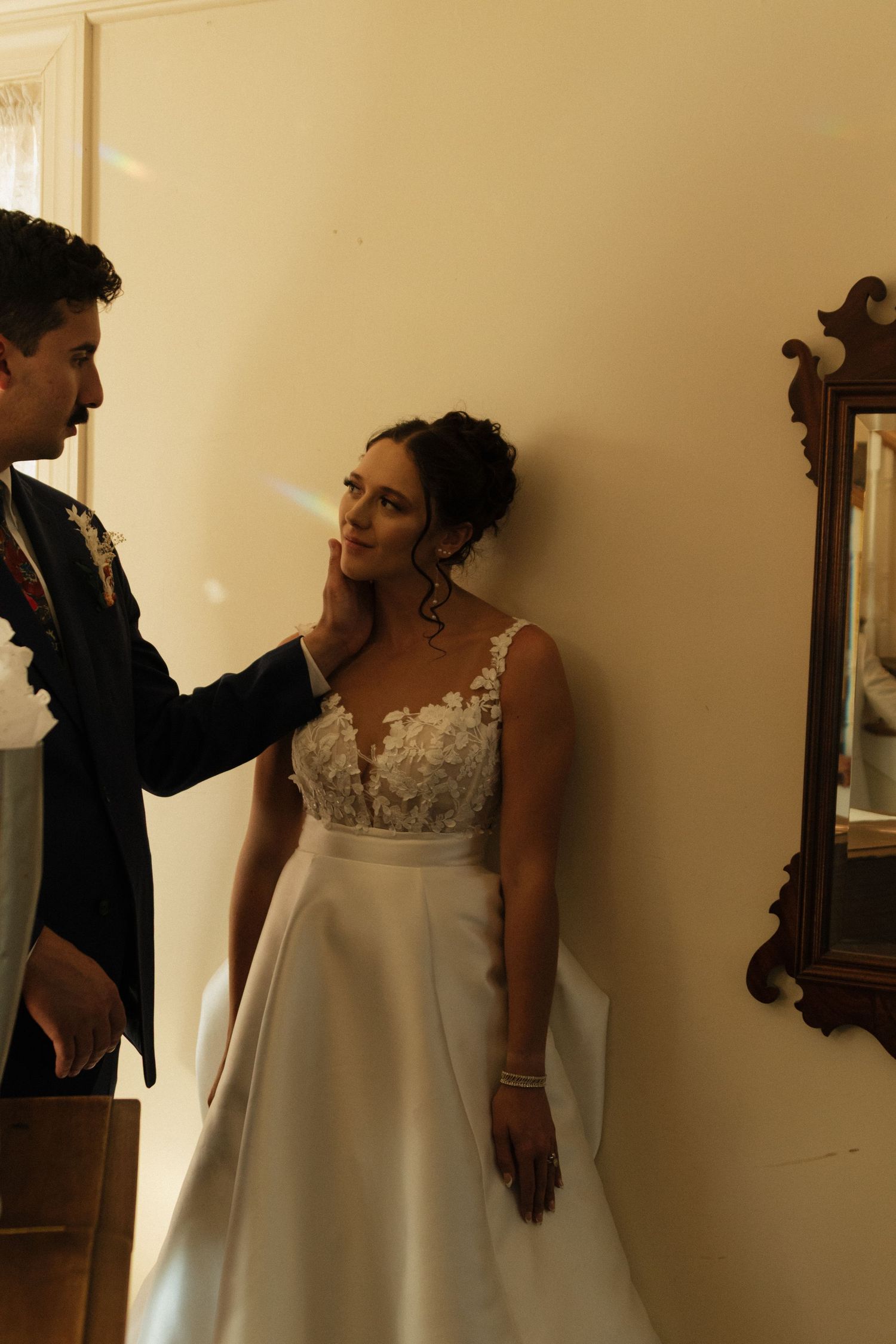 Interior scene showing elegant white wedding dress against beige wall with dramatic window lighting.