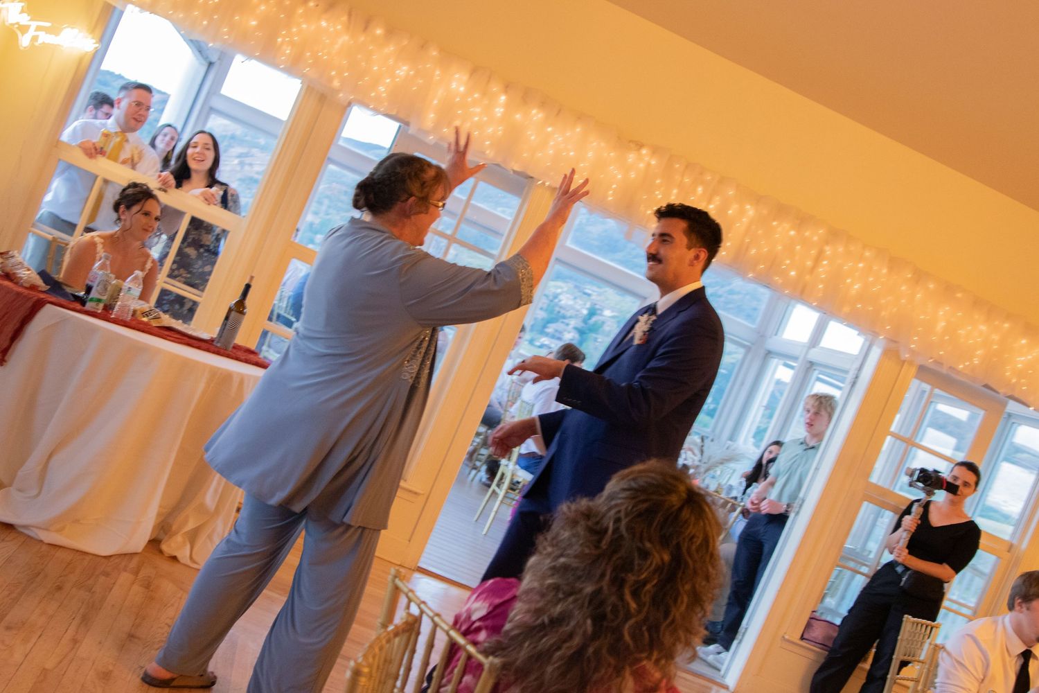 Wedding reception guests dance and celebrate in warmly lit indoor venue.
