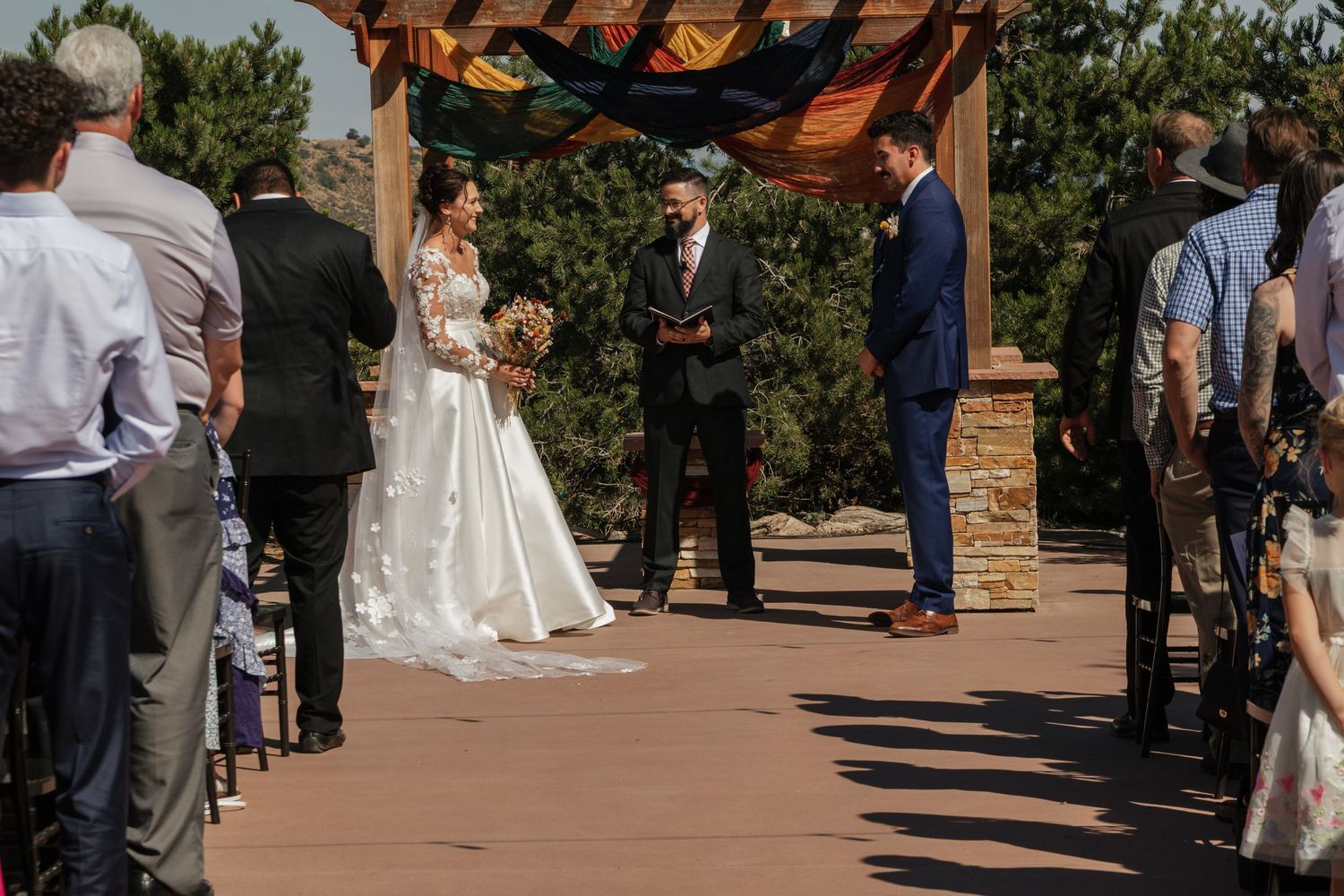 Wedding ceremony taking place under a wooden pergola with mountain scenery in the background.