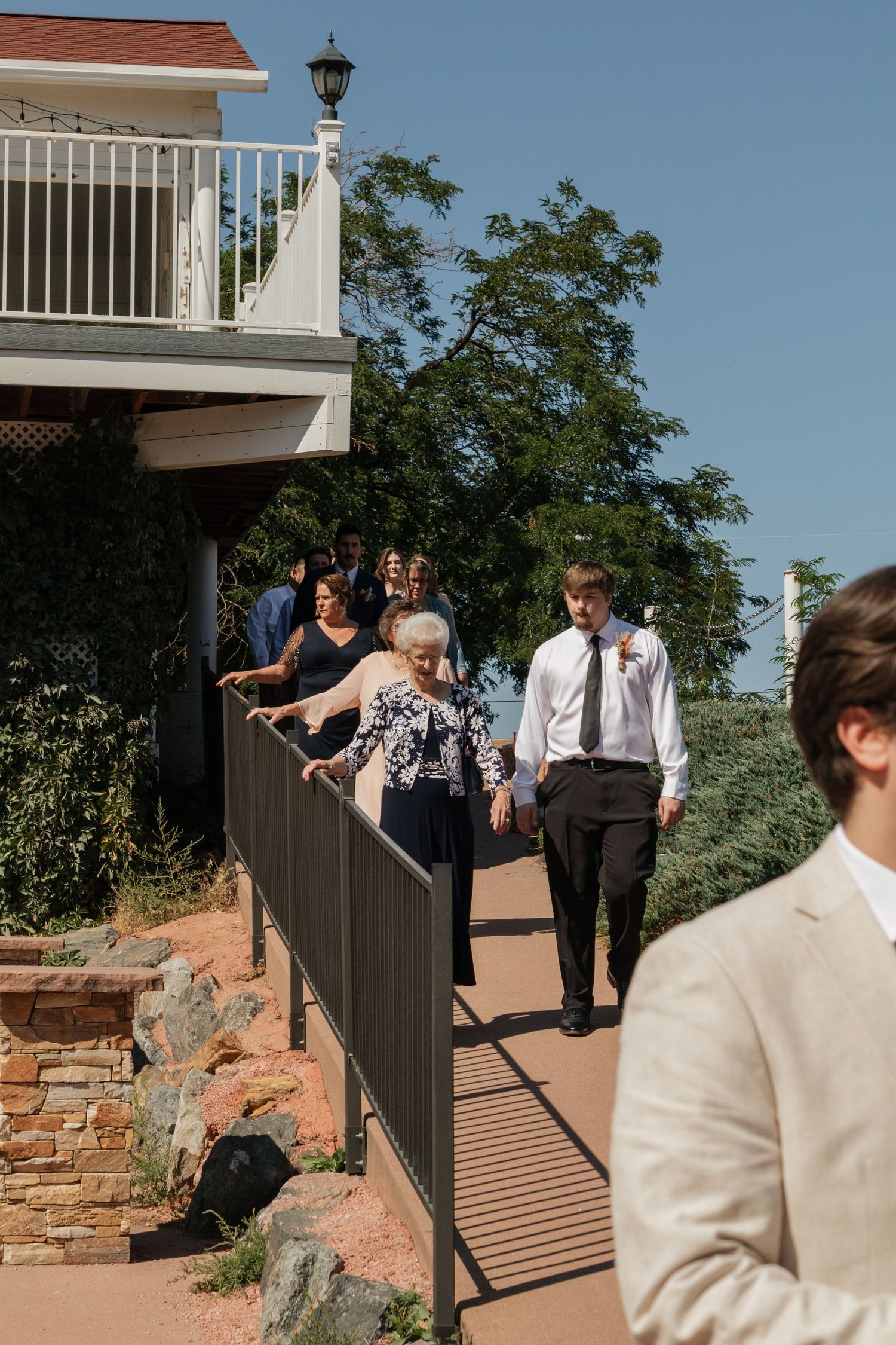A sequence of people walking down exterior stairs at a wedding venue on a sunny day.