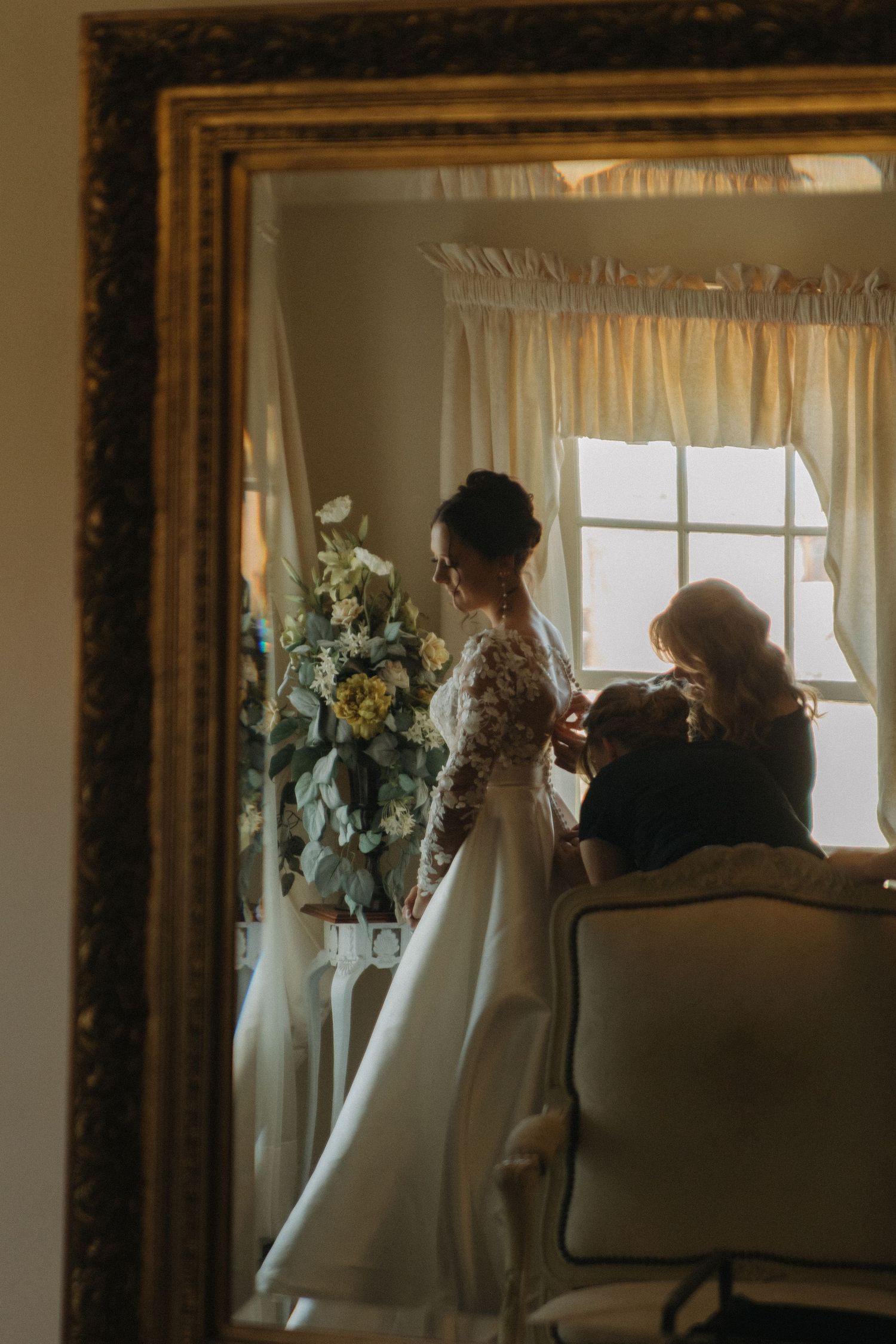 A group gathers by a window with floral arrangements and soft natural lighting.