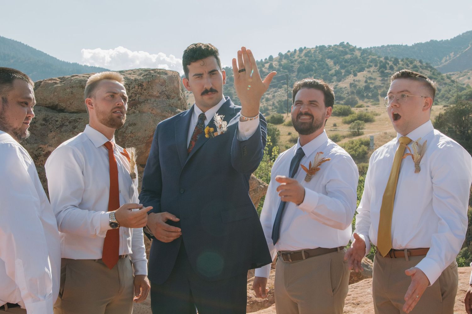 Groomsmen in white shirts and ties performing synchronized gestures at an outdoor wedding.