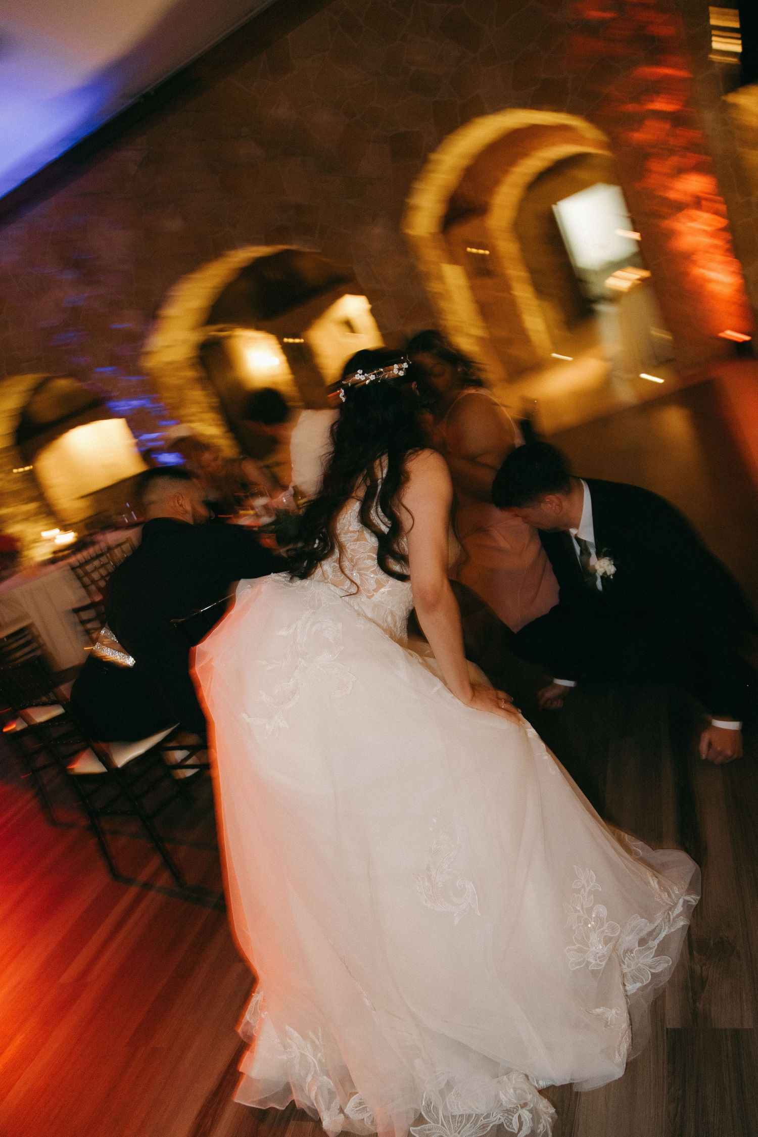 Motion-blurred photo of bride and groom spinning on the dance floor in a stone-arched wedding venue.