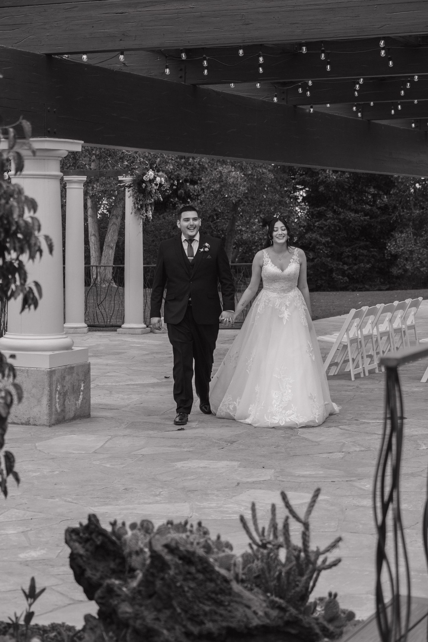 Black and white photo of newlyweds walking hand in hand after outdoor wedding ceremony.