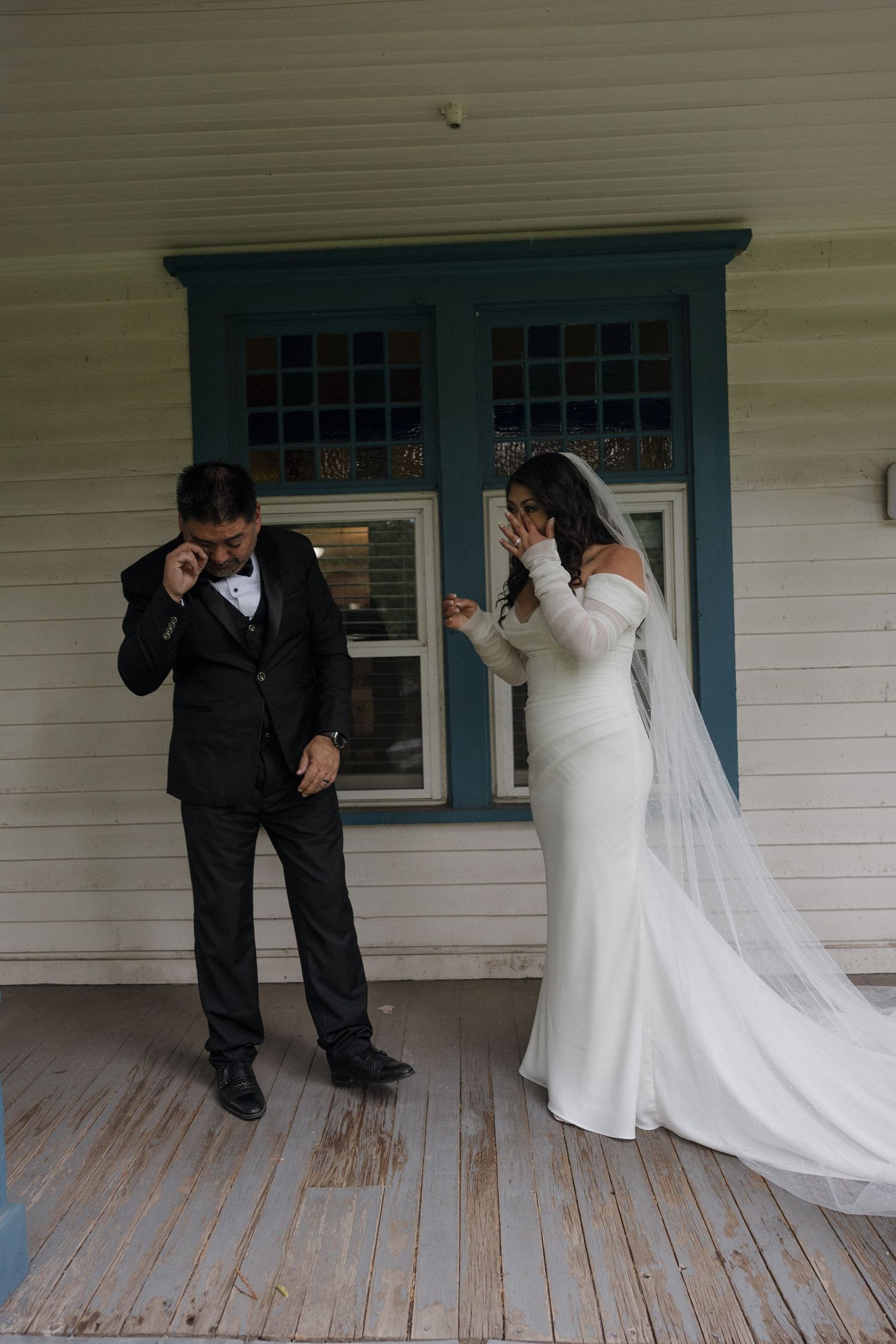 Emotional bride and groom share first look moment on vintage home porch, both wiping tears of joy.