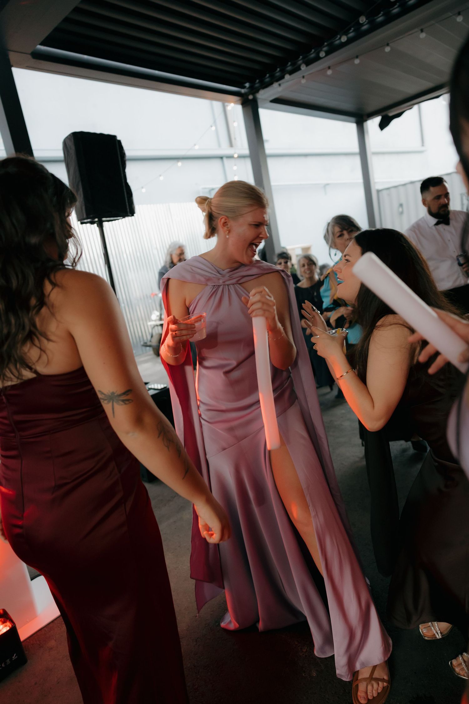Wedding guests in purple and burgundy dresses dancing joyfully with glow sticks at reception.