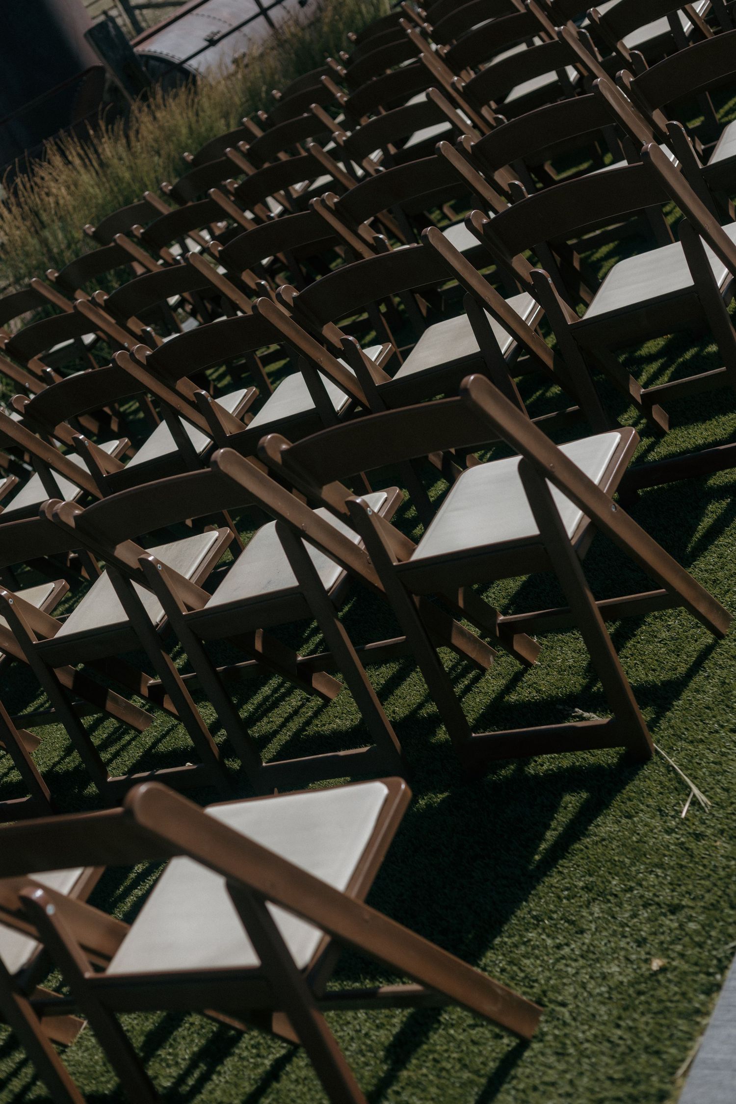 Rows of wooden folding chairs with white cushions arranged on green grass for an outdoor wedding ceremony.