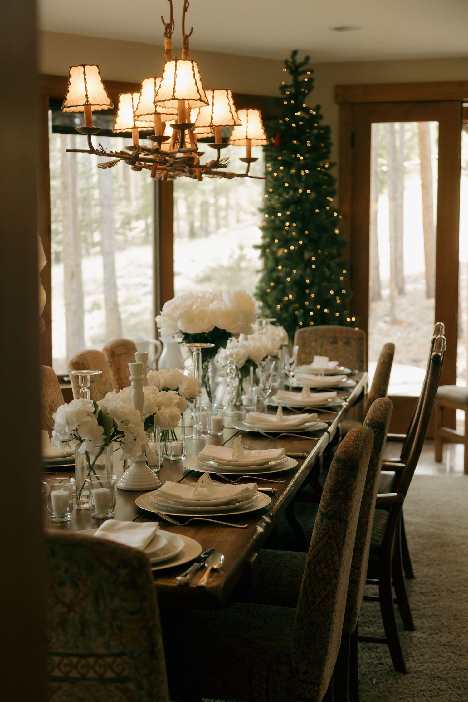 Elegant winter wedding reception table with white florals, chandelier, and Christmas tree backdrop.