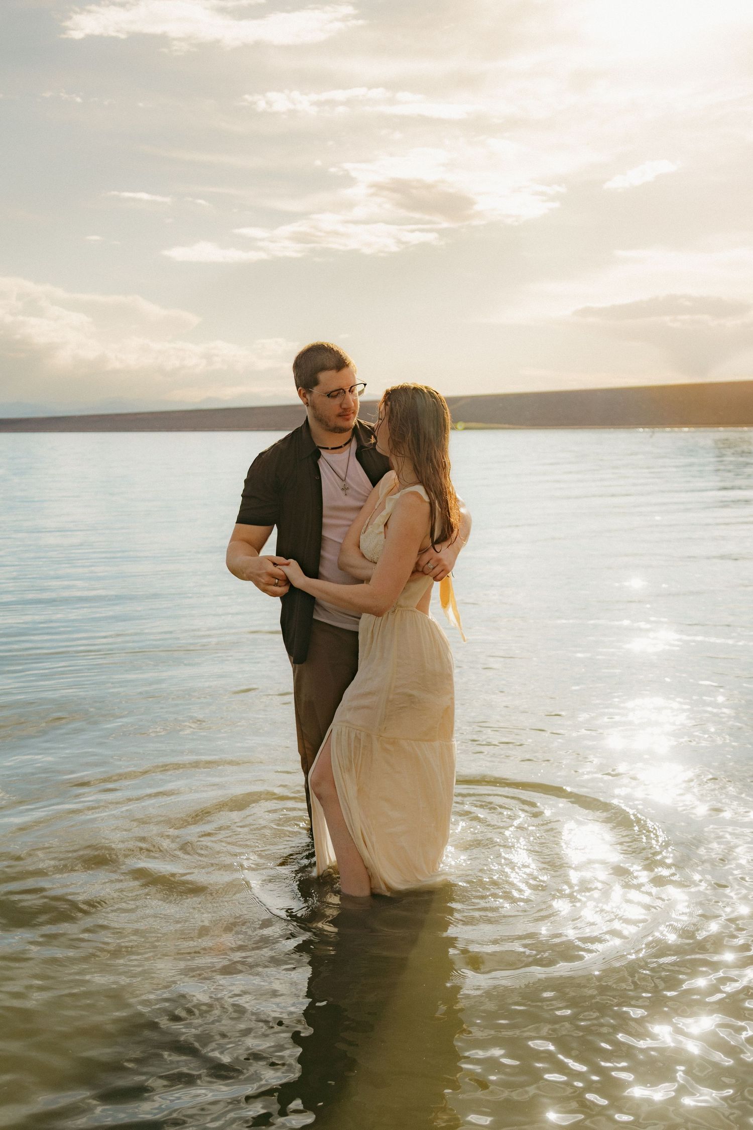 Romantic couple embracing while standing in a shallow lake during a golden sunset.
