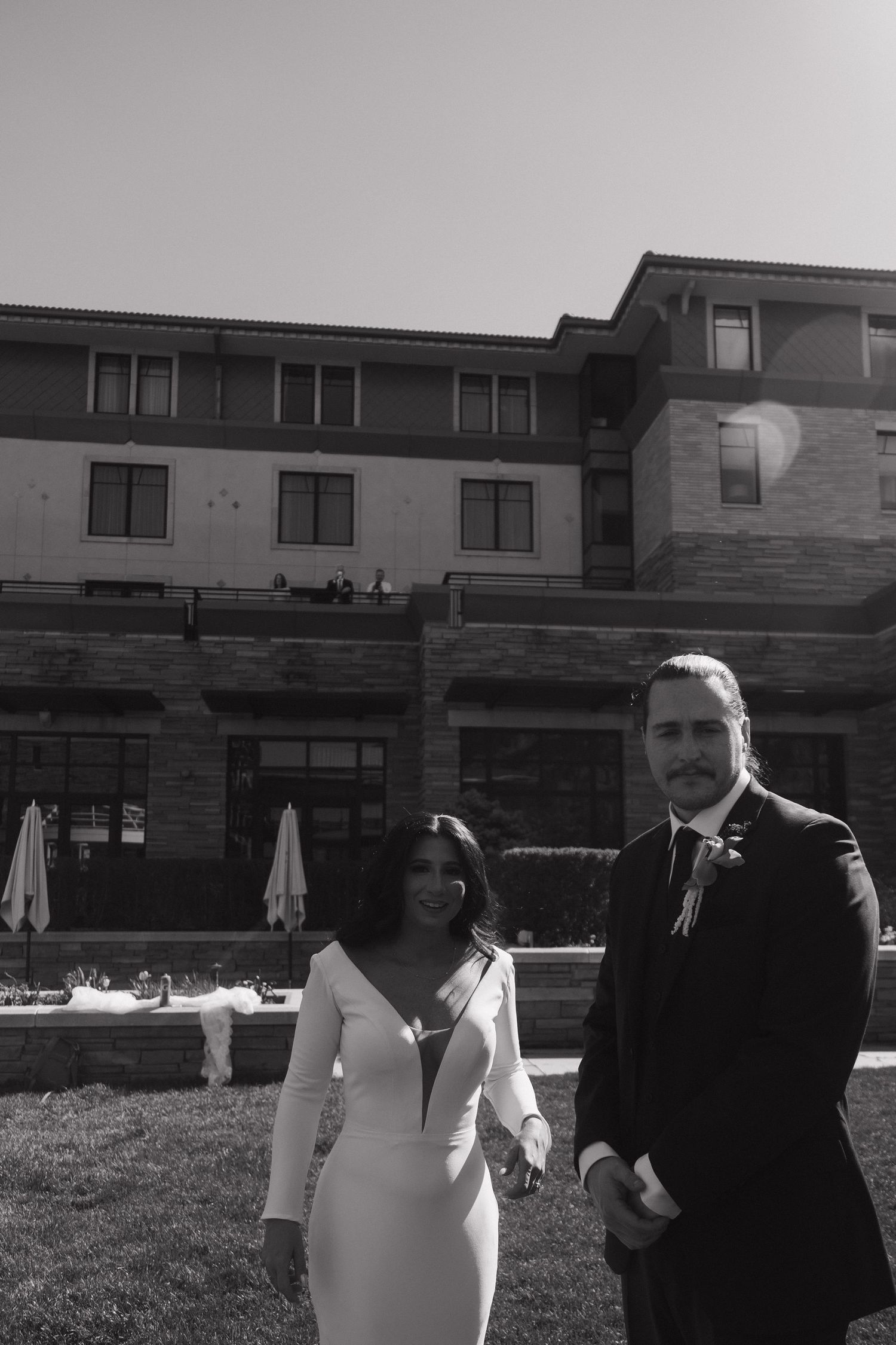 Black and white photo of bride and groom standing together on lawn outside elegant venue.