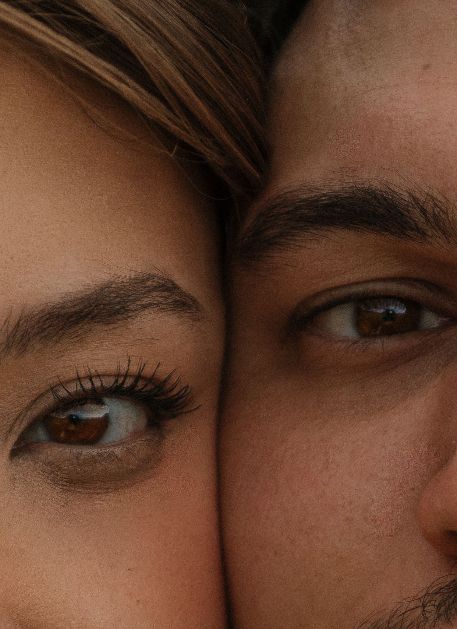 Close-up portrait of a couple with foreheads together, showing their brown eyes in detail.