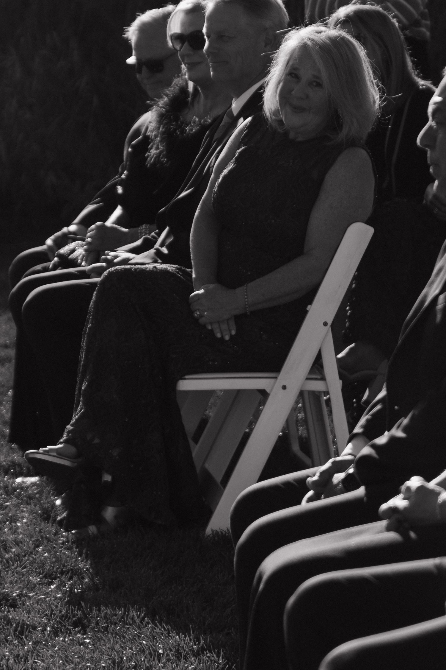 Black and white image showing white folding chairs arranged for an outdoor wedding ceremony.