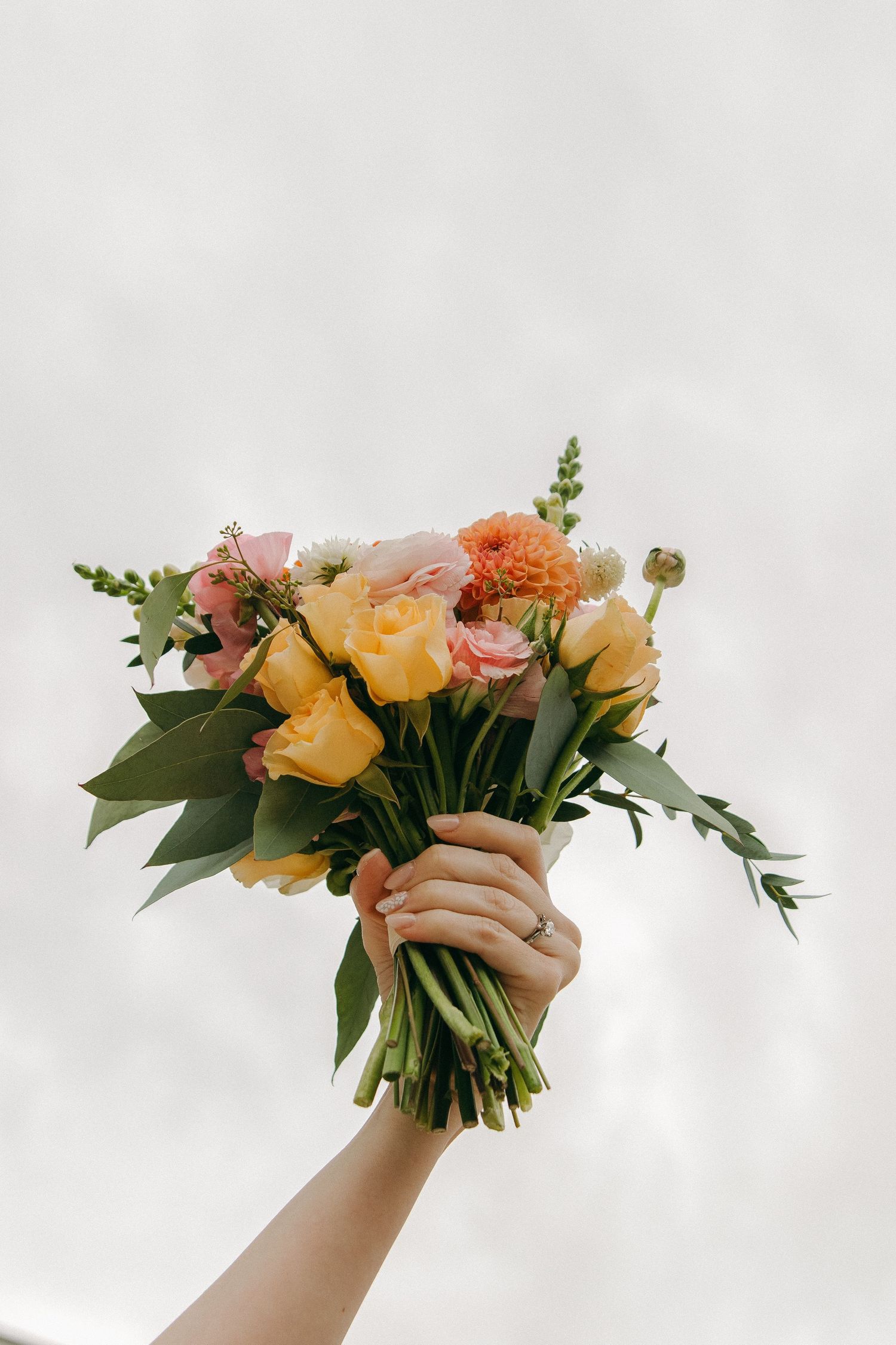 Hands holding colorful floral bouquets with roses and mixed flowers against a white background.