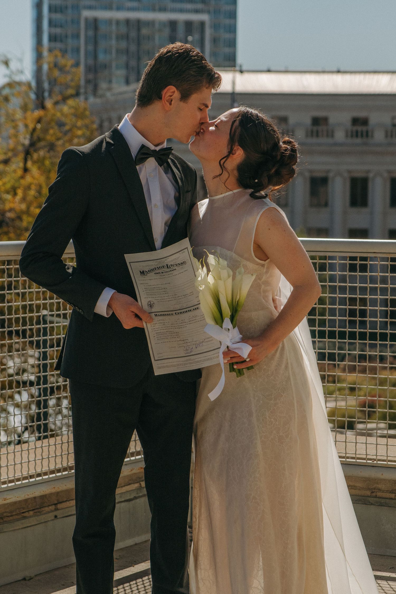 Newlyweds sharing a romantic moment on an outdoor terrace with city buildings in background.