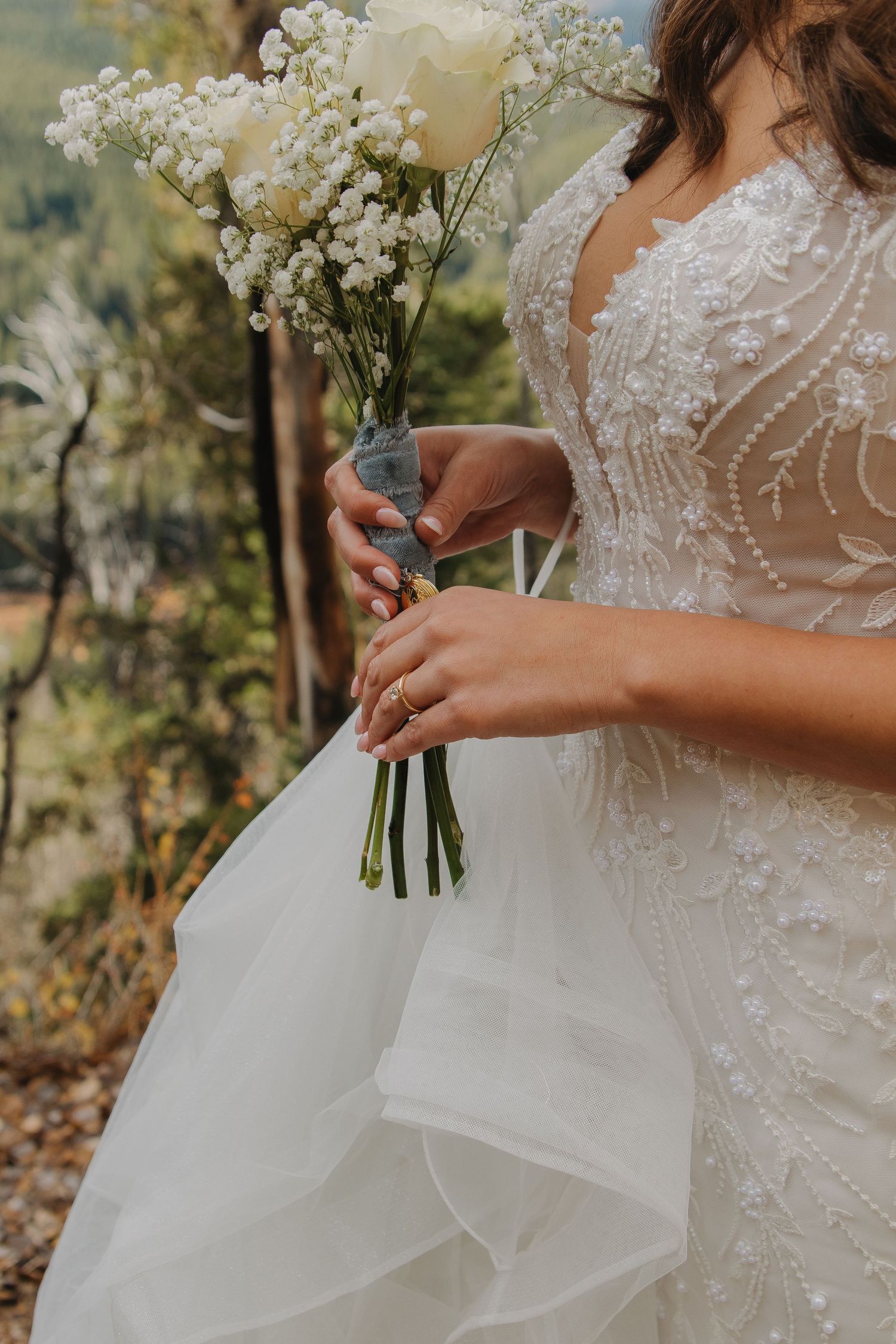 Close-up detail of a white wedding dress with baby's breath bouquet against mountain scenery.