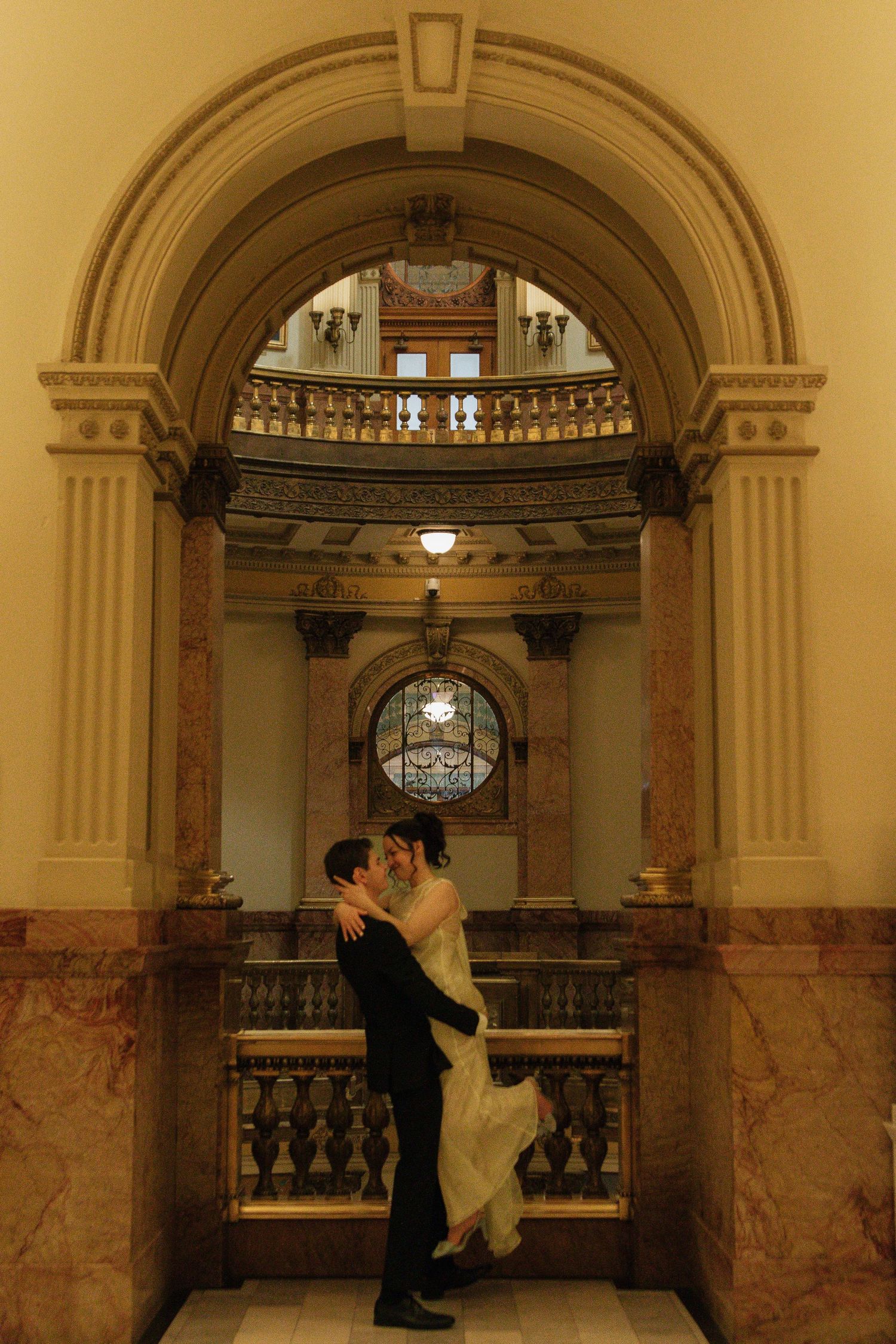 A romantic moment captured in a grand marble hallway with ornate architectural details and arches.