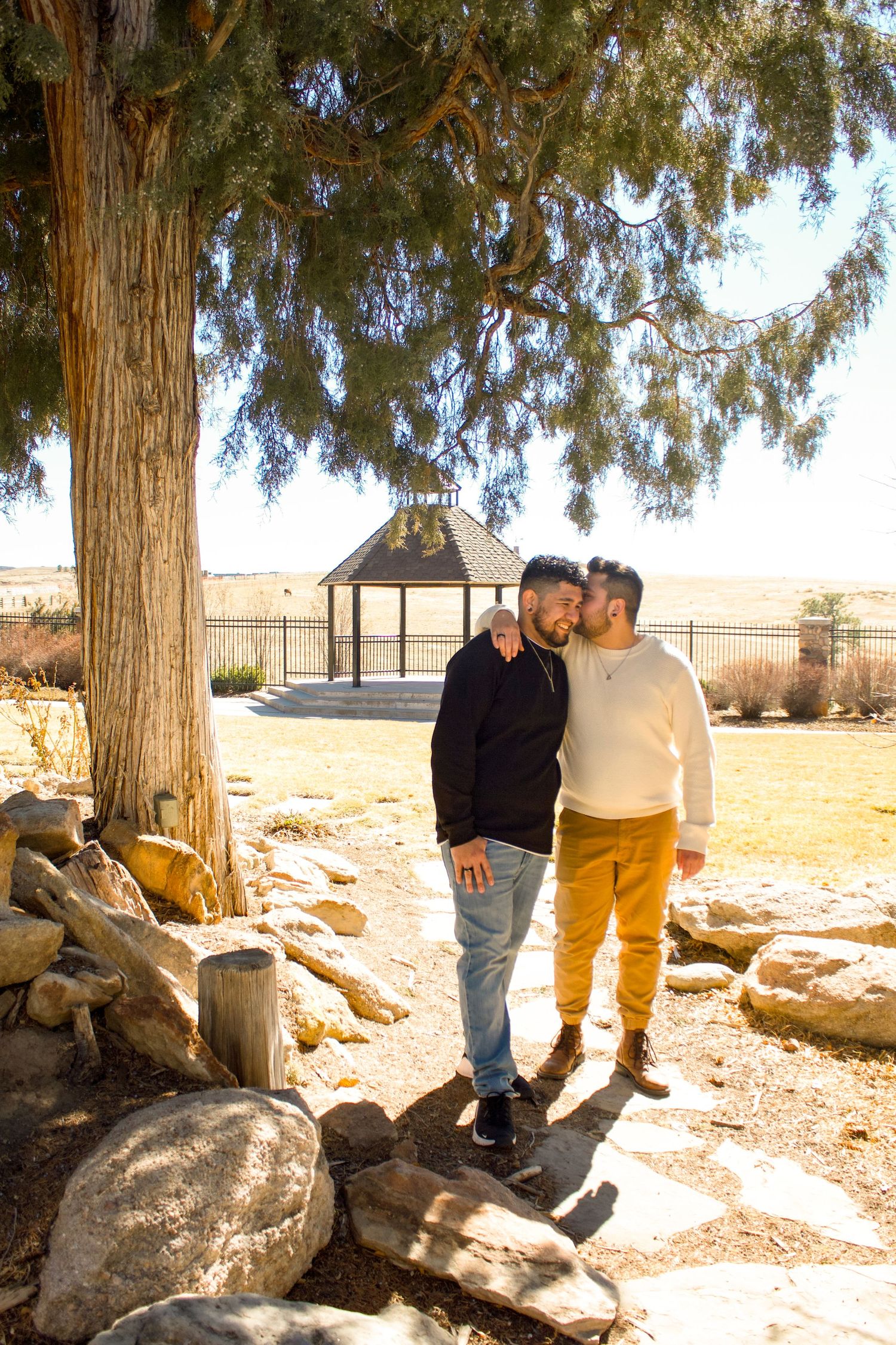 Couple walking together under large tree with gazebo in background.