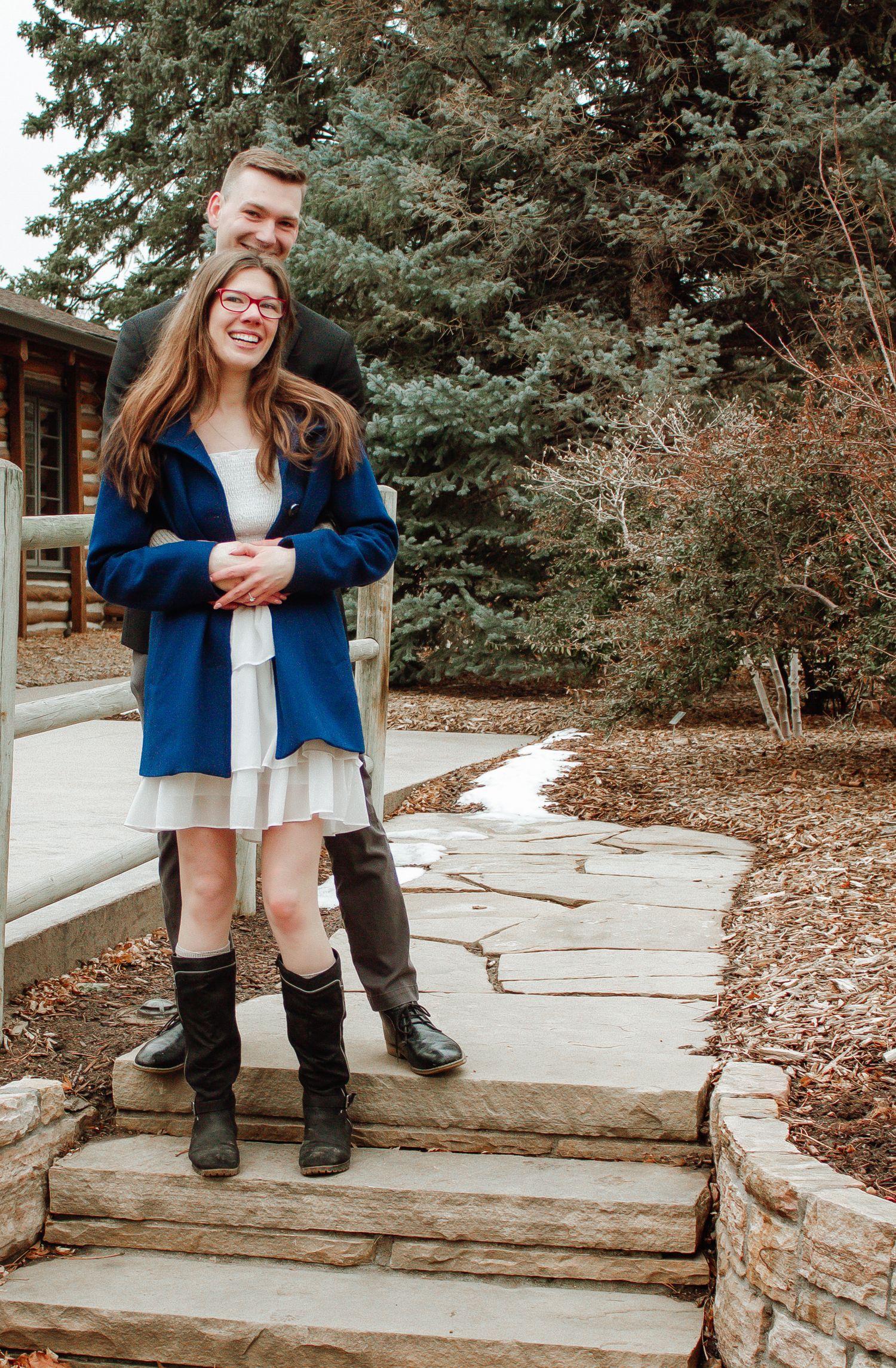 A couple shares a sweet moment together on stone steps surrounded by evergreen trees.