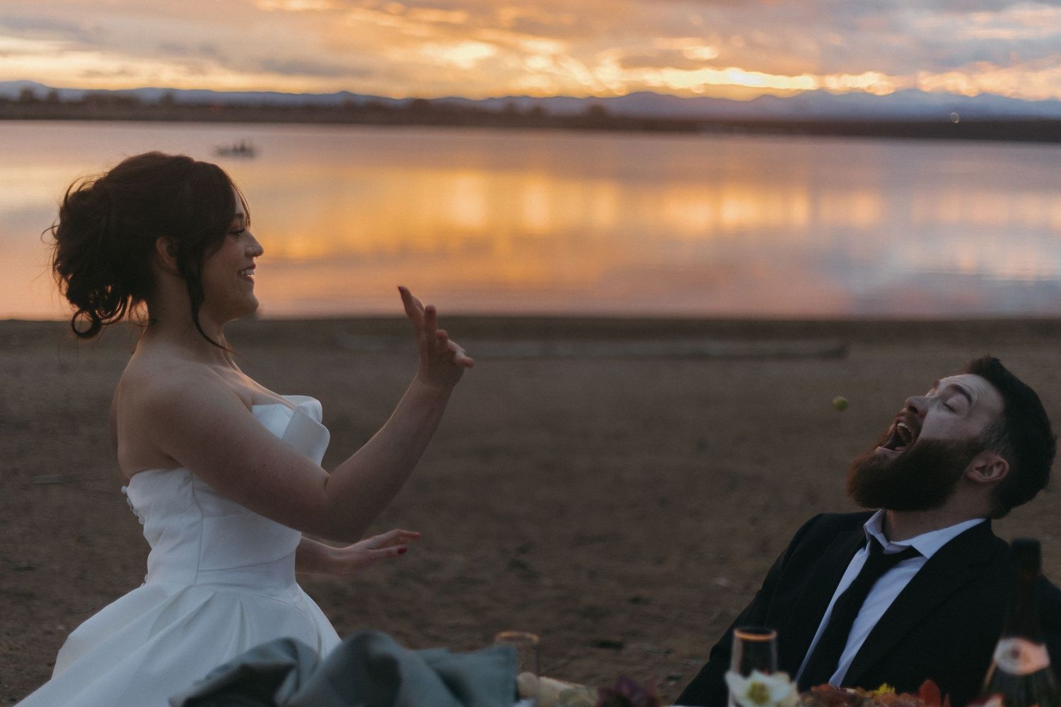 A playful sunset moment between newlyweds on a beach with dramatic orange sky reflections.