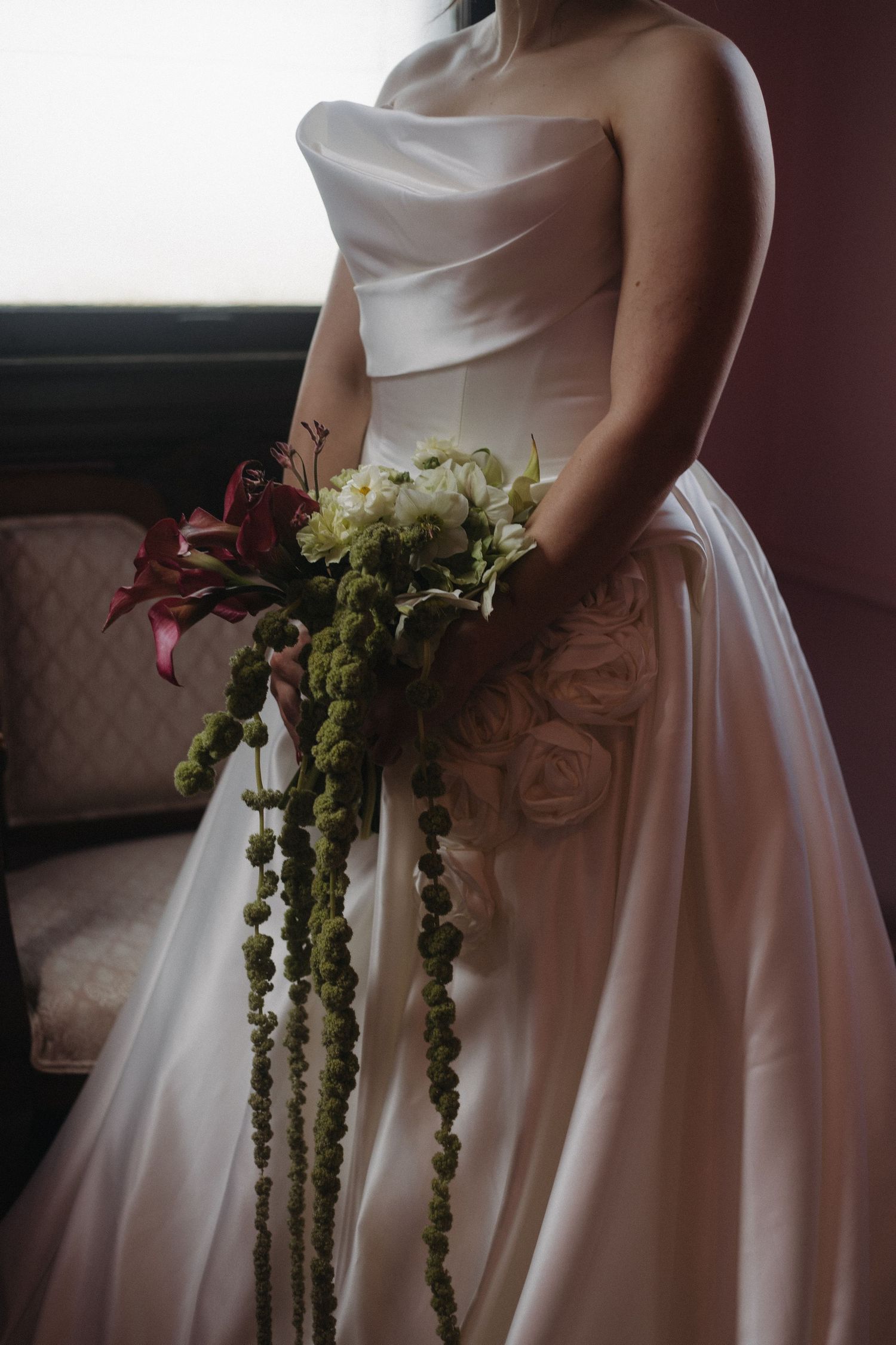 Close-up of white wedding dress with cascading green floral bouquet details.