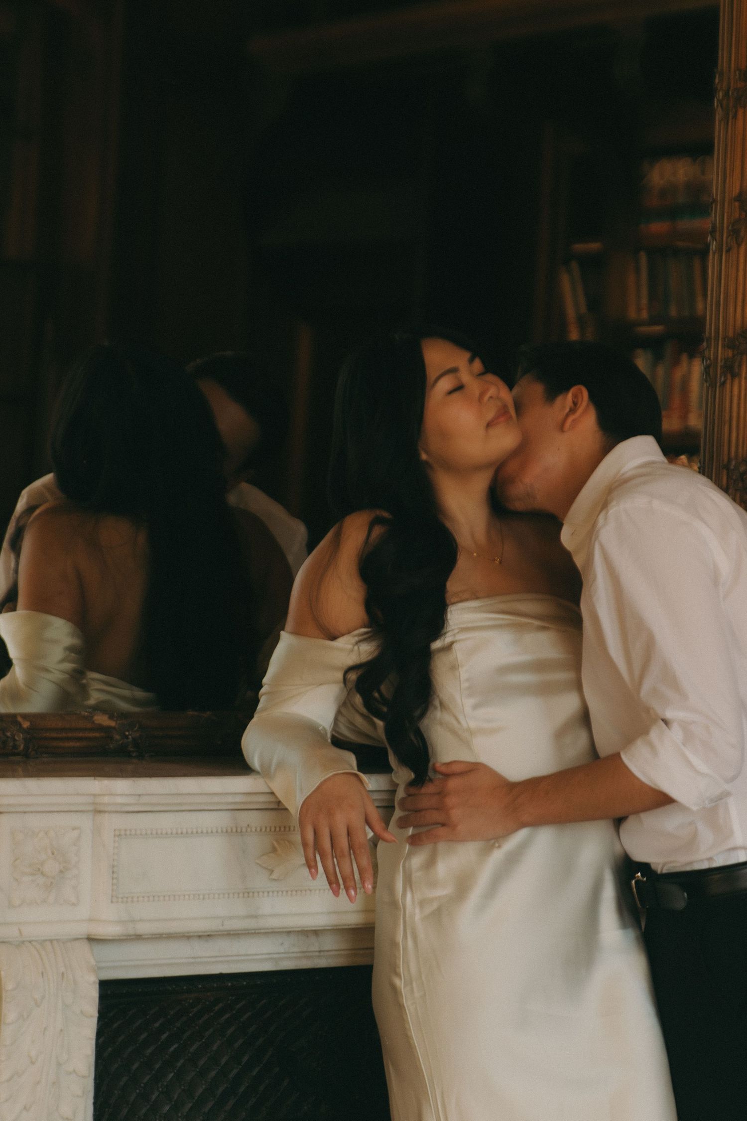 Intimate moment captured against mirror and bookshelf backdrop in vintage setting.