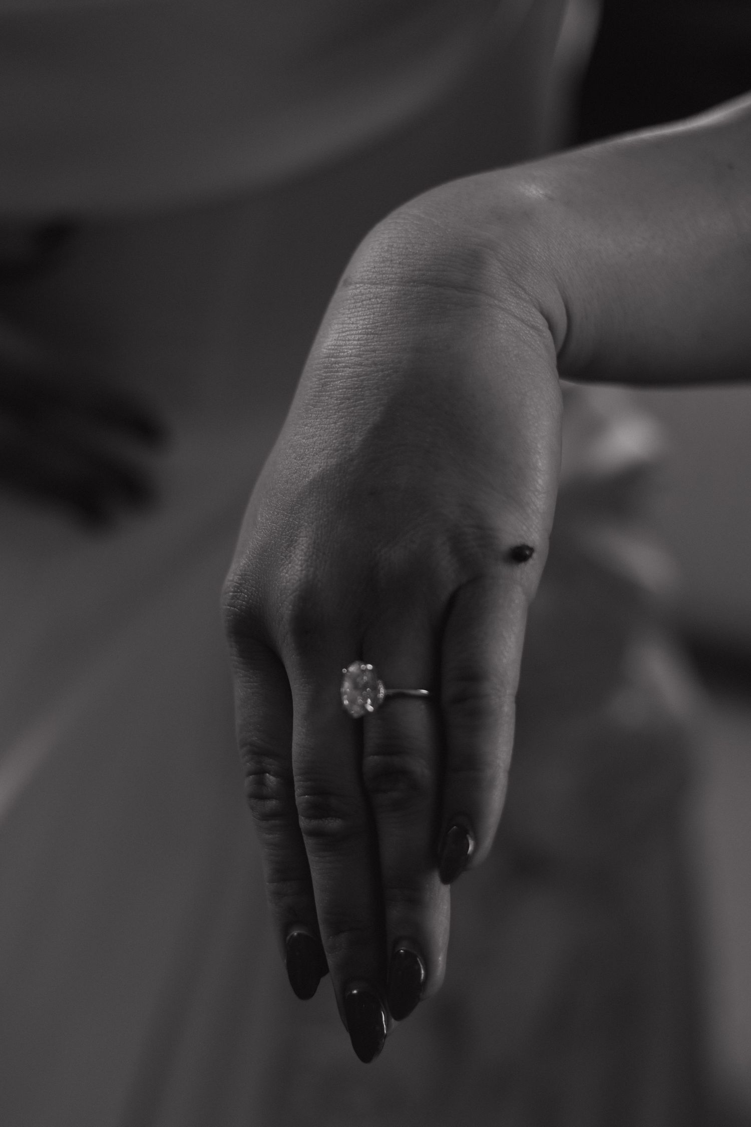 Close-up black and white photograph of a hand wearing an engagement ring.