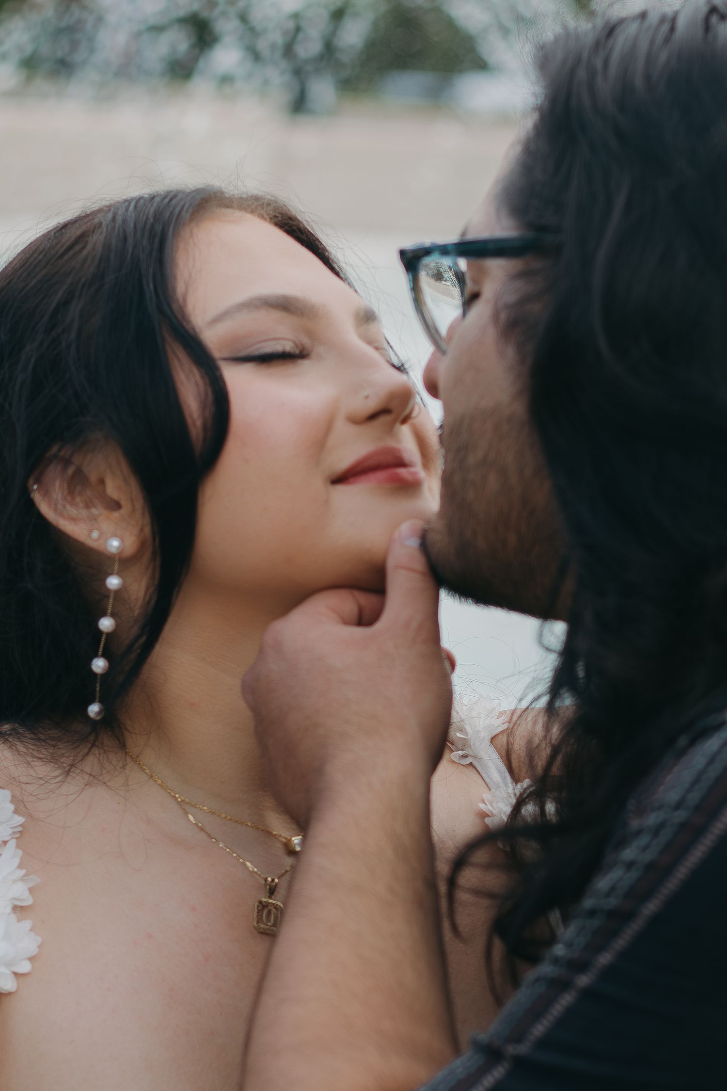Intimate moment captured between couple with dangling pearl earrings and dark clothing.