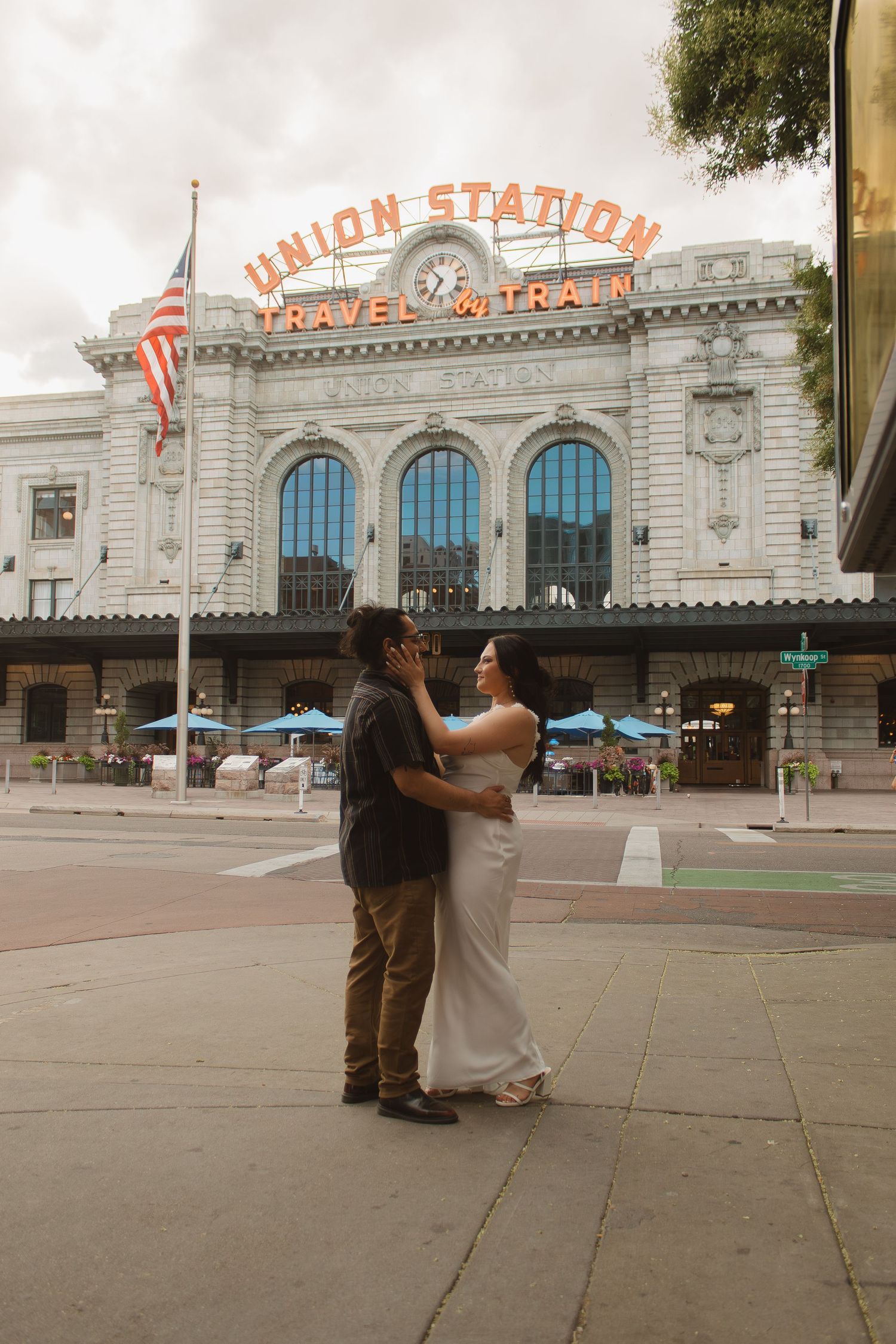 A romantic embrace outside Denver's Union Station with American flag and illuminated signage in background.