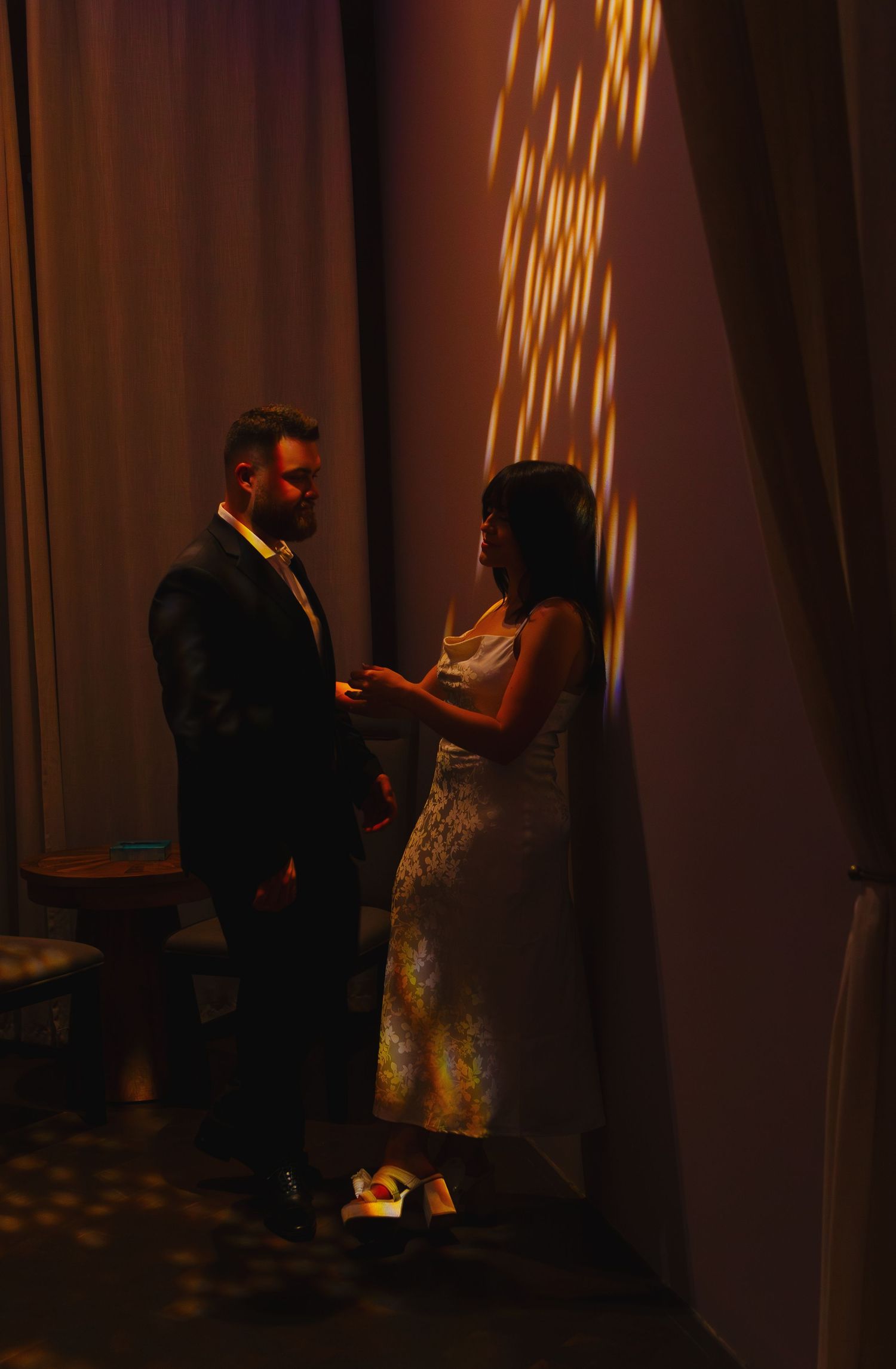 A couple shares an intimate dance moment in dim lighting with glowing curtains behind them.