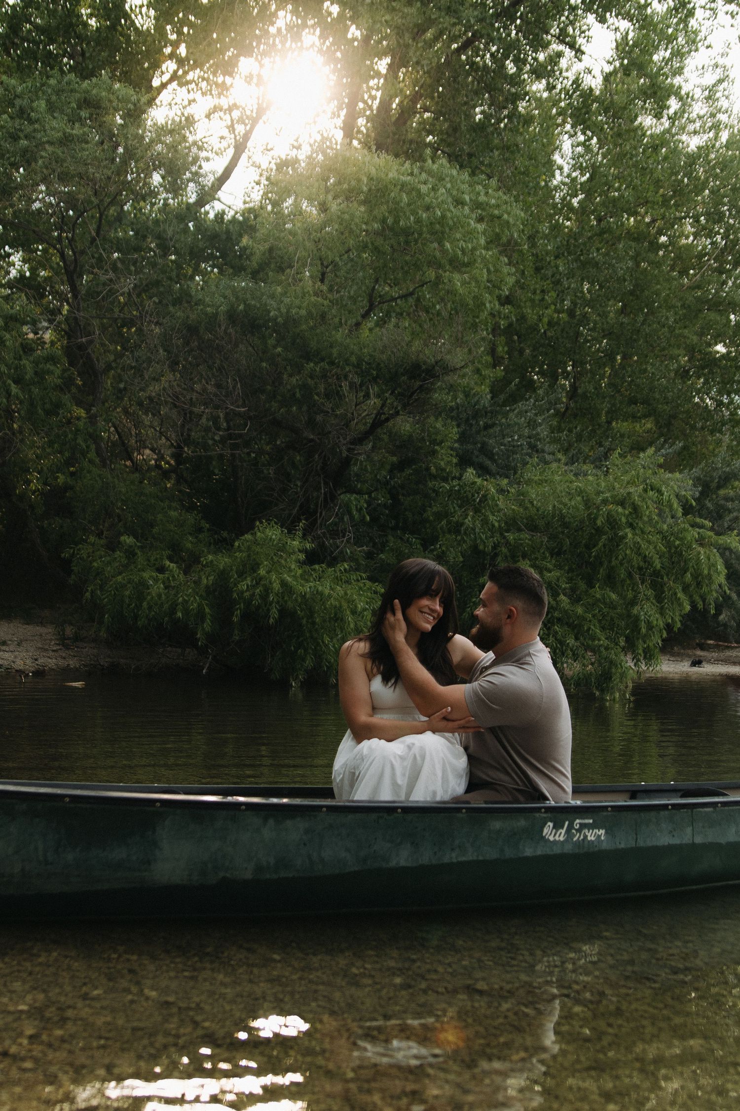 Romantic couple sitting in a canoe surrounded by lush greenery and sunlight.