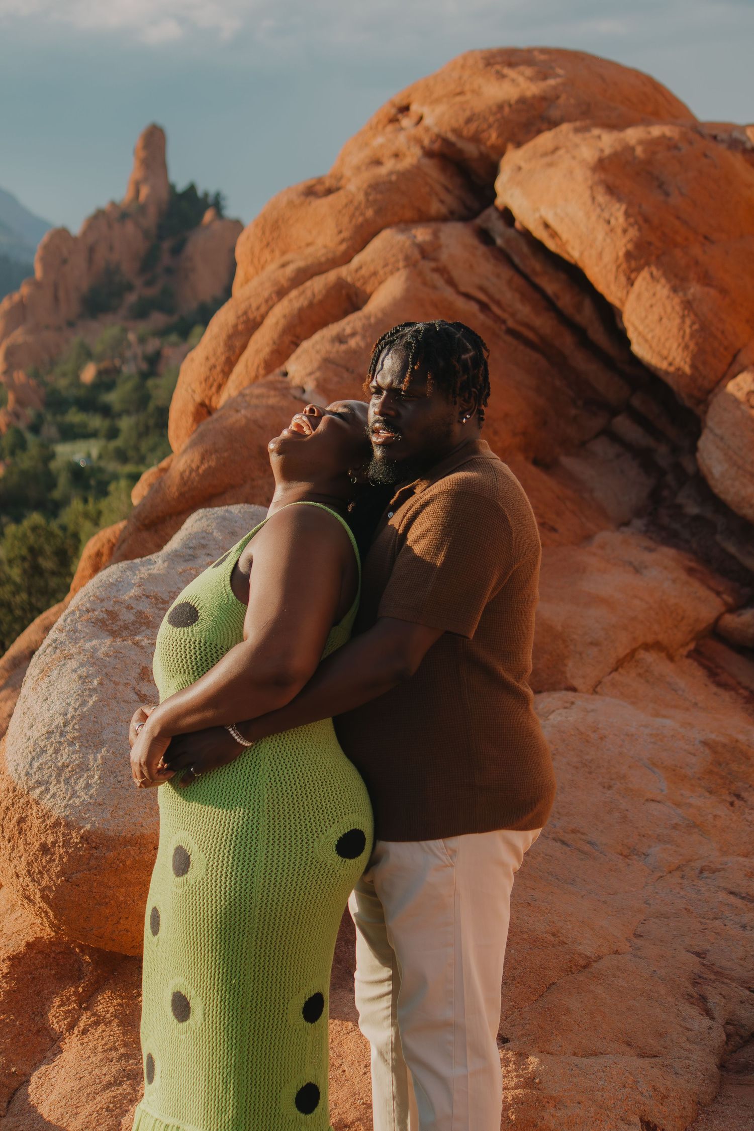 Two figures in lime green and brown embracing against red rock formations at sunset.