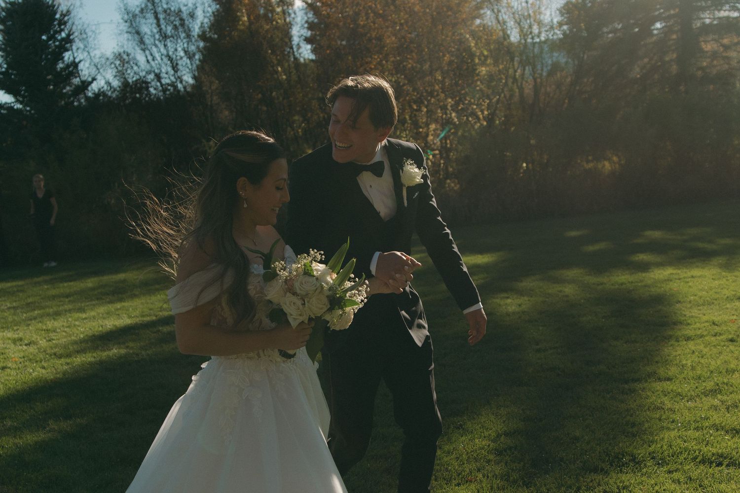A couple in wedding attire stands together in a sunlit garden setting during an outdoor autumn ceremony.