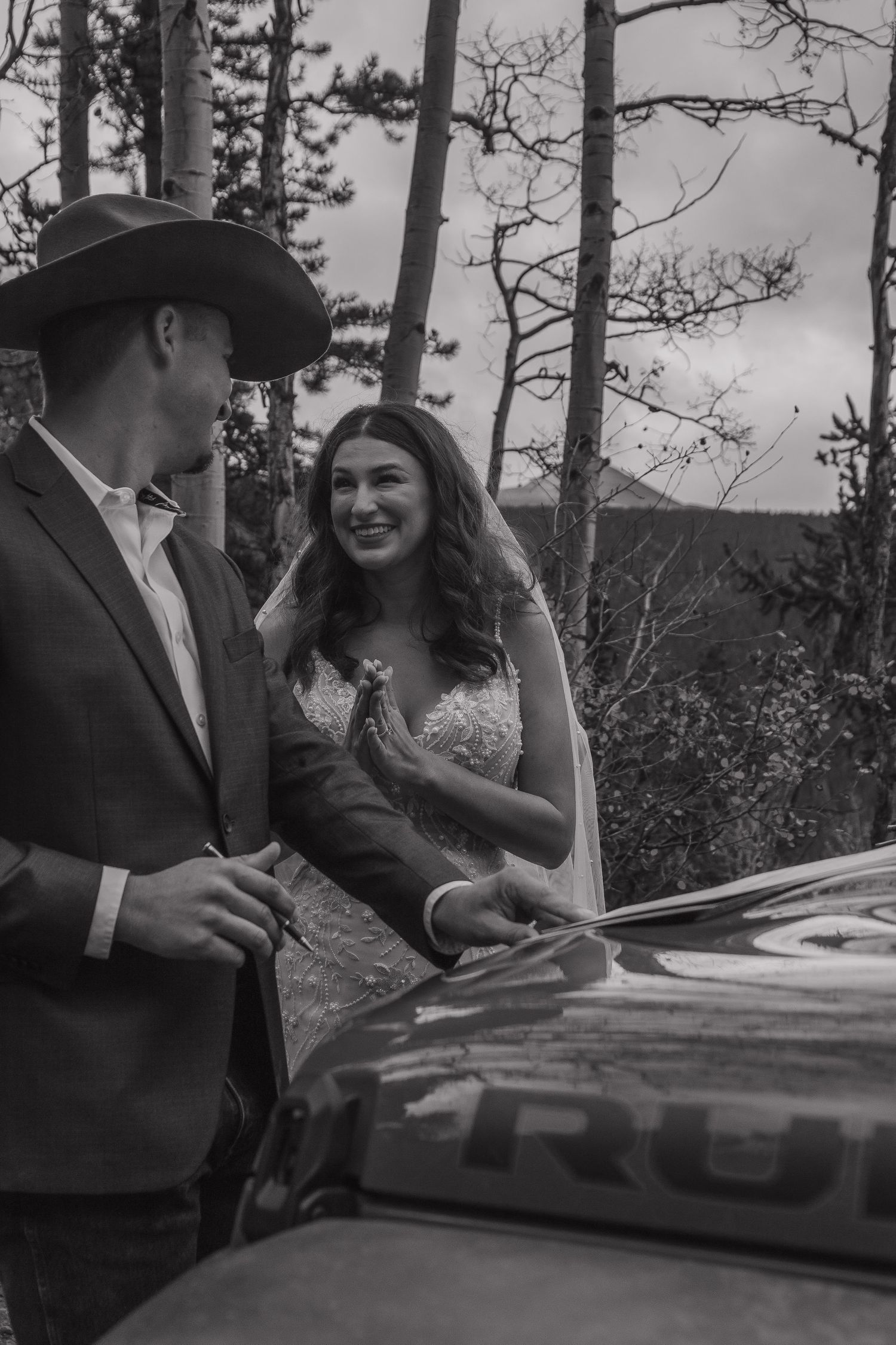 Black and white photo showing a couple signing documents outdoors among tall pine trees.