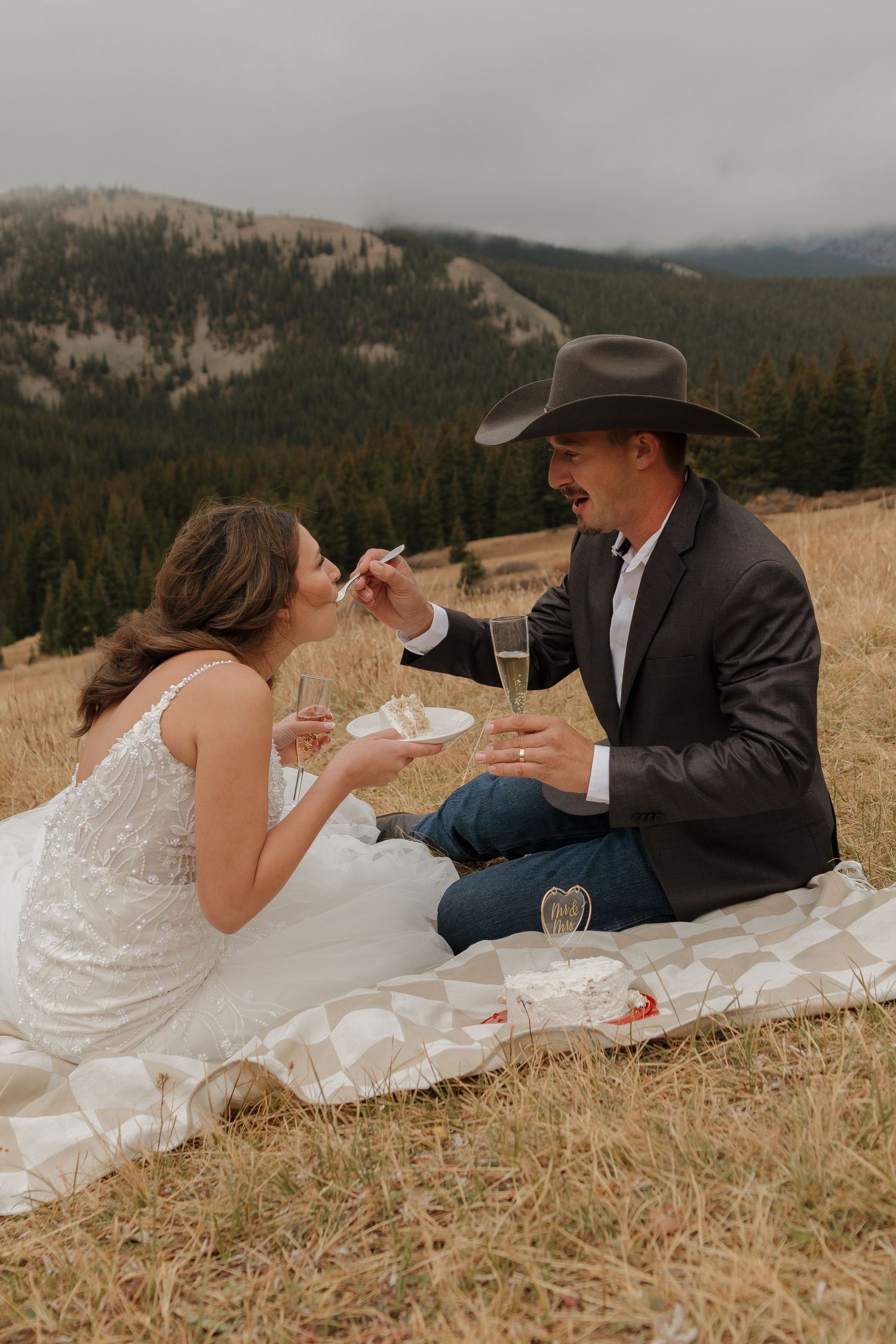 A couple shares champagne while relaxing in a mountain meadow.