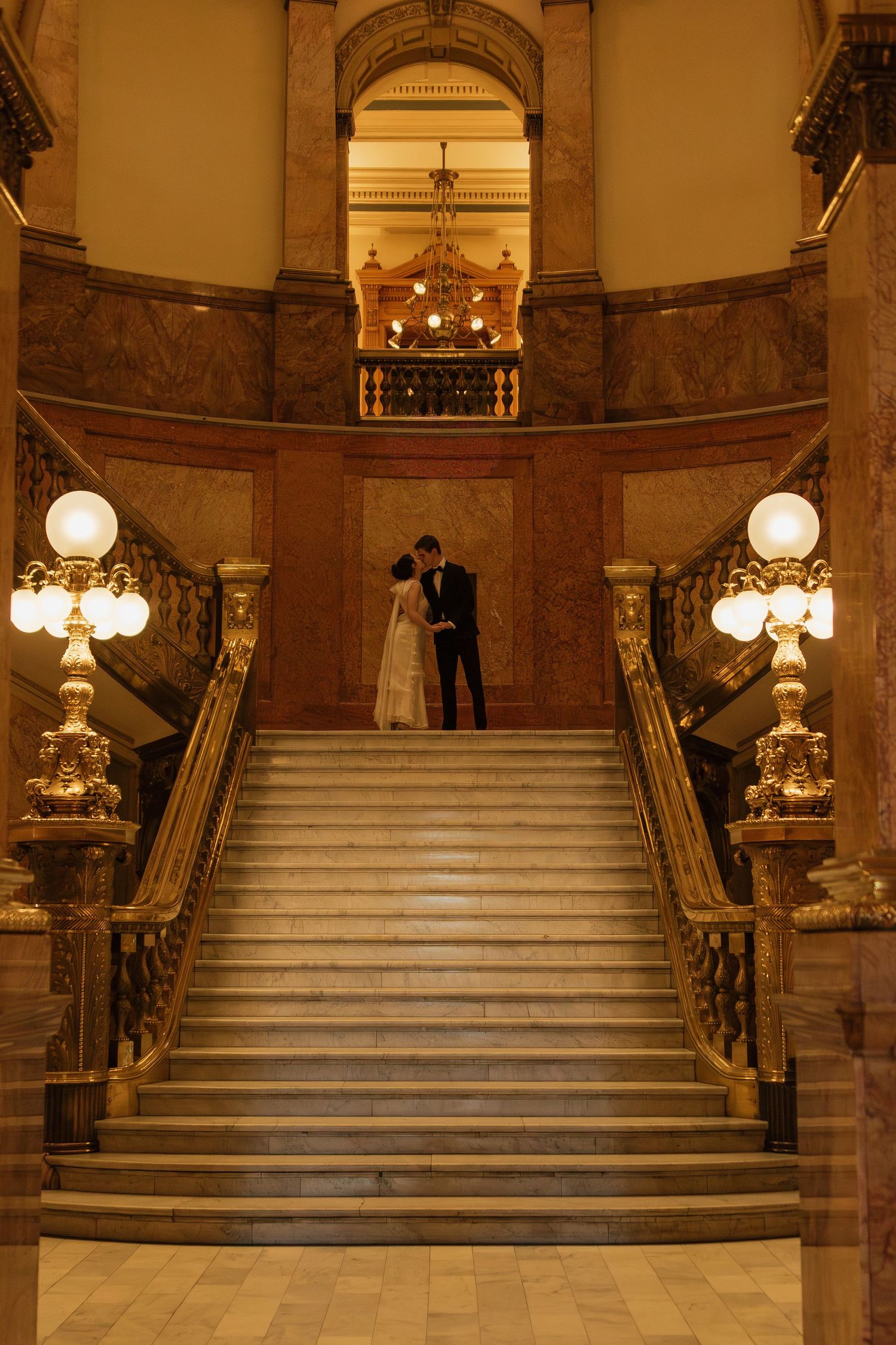 Elegant marble staircase in a grand historic building with ornate lighting fixtures and architectural details.