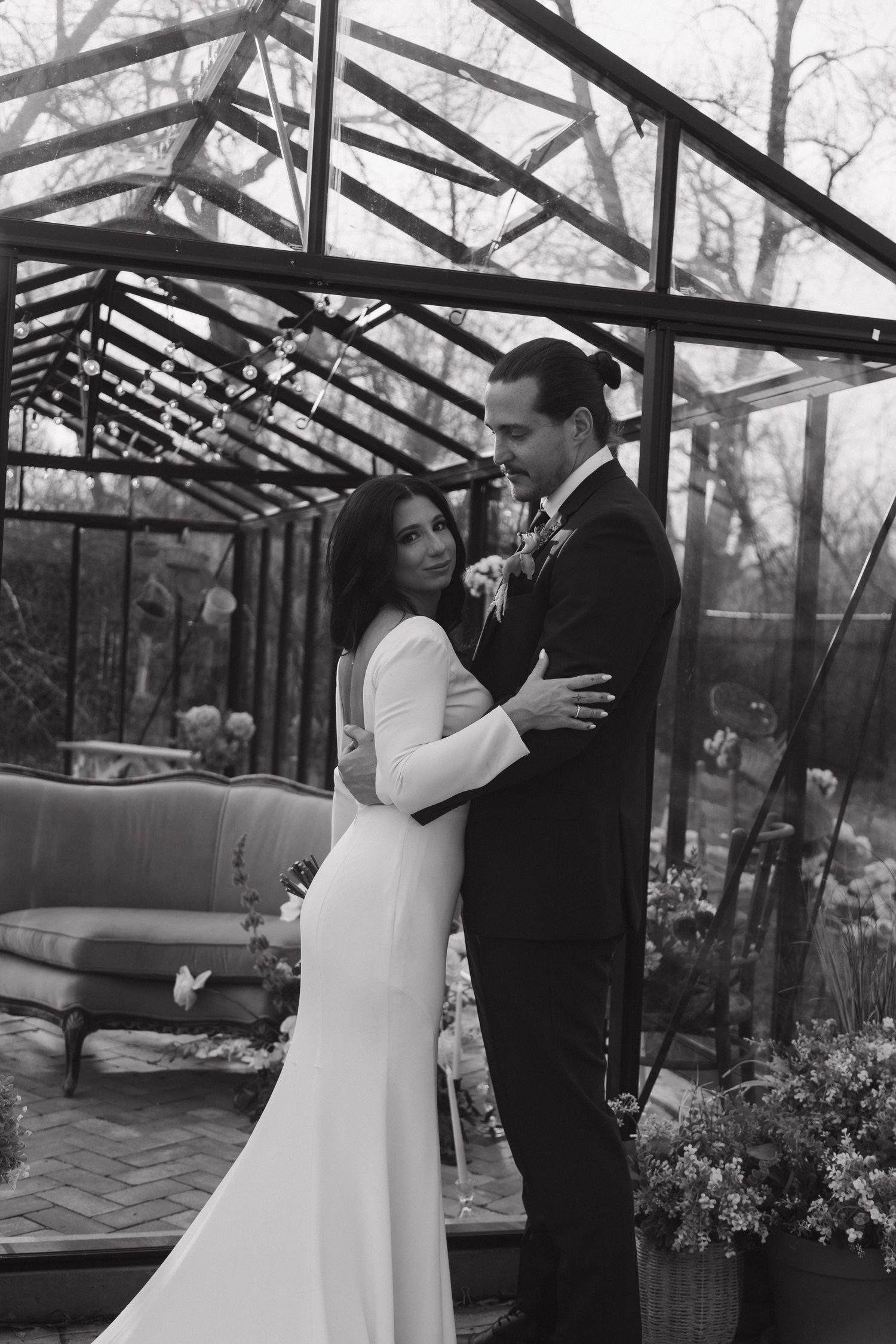 Black and white photo of bride and groom embracing romantically inside a glass greenhouse wedding venue.