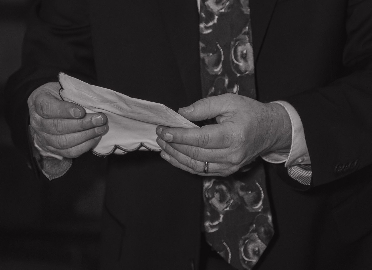 Black and white photo of a man in suit and tie holding a folded cloth or handkerchief in both hands.